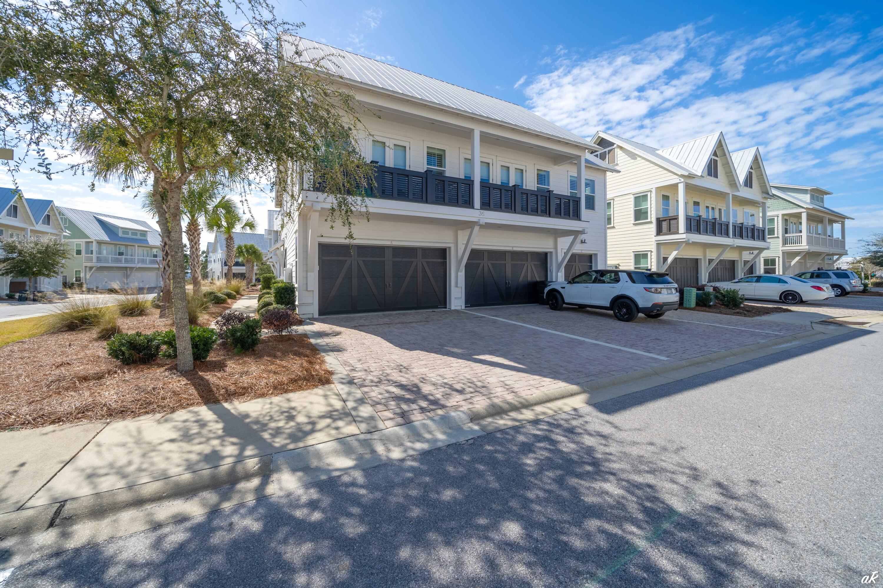 White coastal-style home with a metal roof, dark balcony railing, and two garage doors.