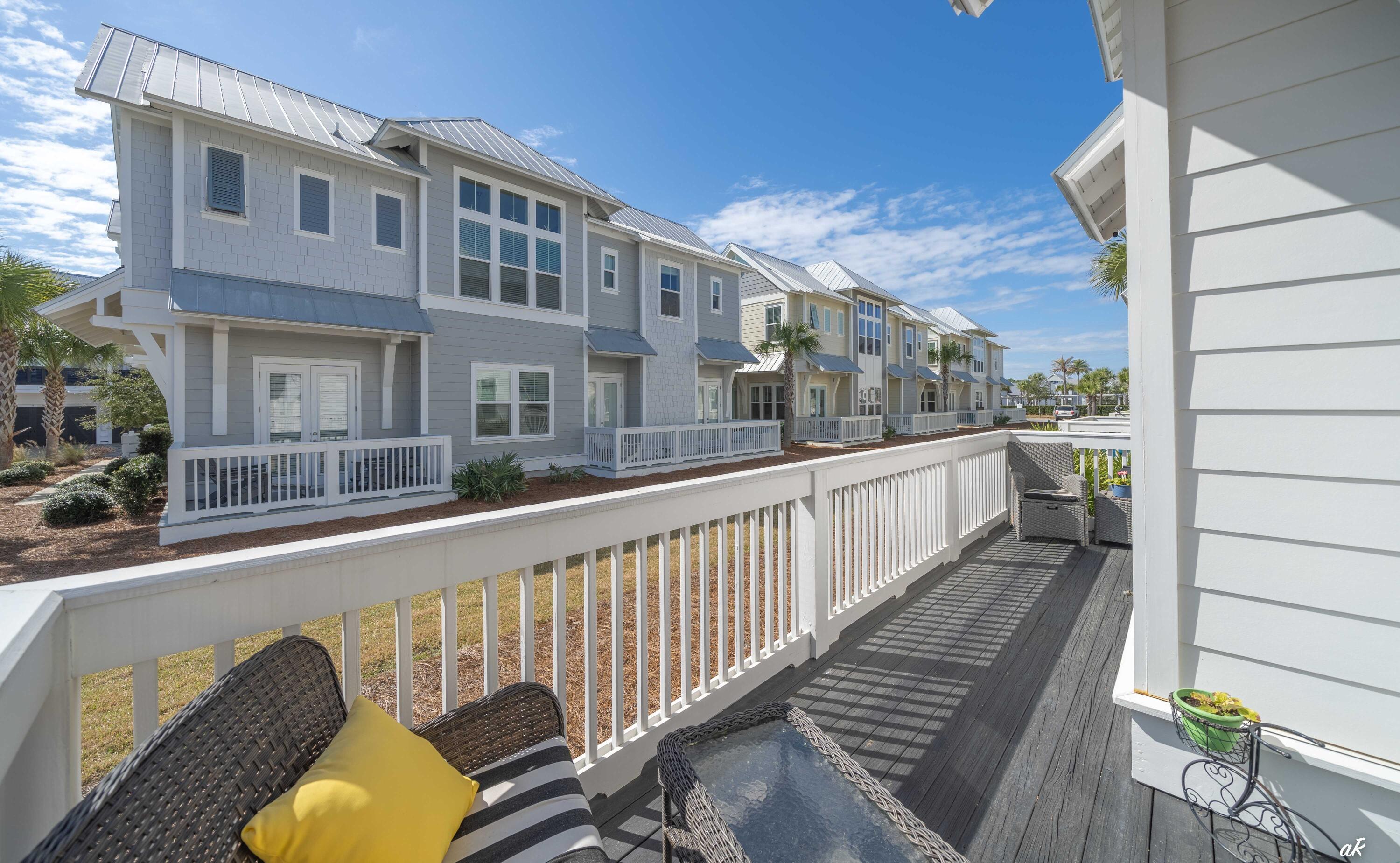 Furnished deck overlooking gray coastal townhomes, with white railings and wicker seating.