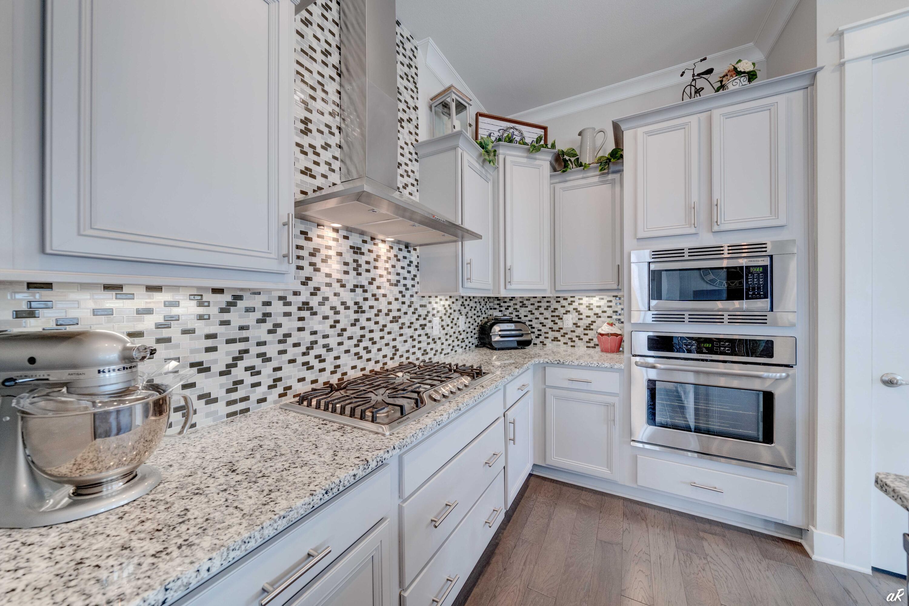 Bright kitchen with white cabinetry, mosaic tile backsplash, granite counters, gas cooktop, and stainless steel appliances.