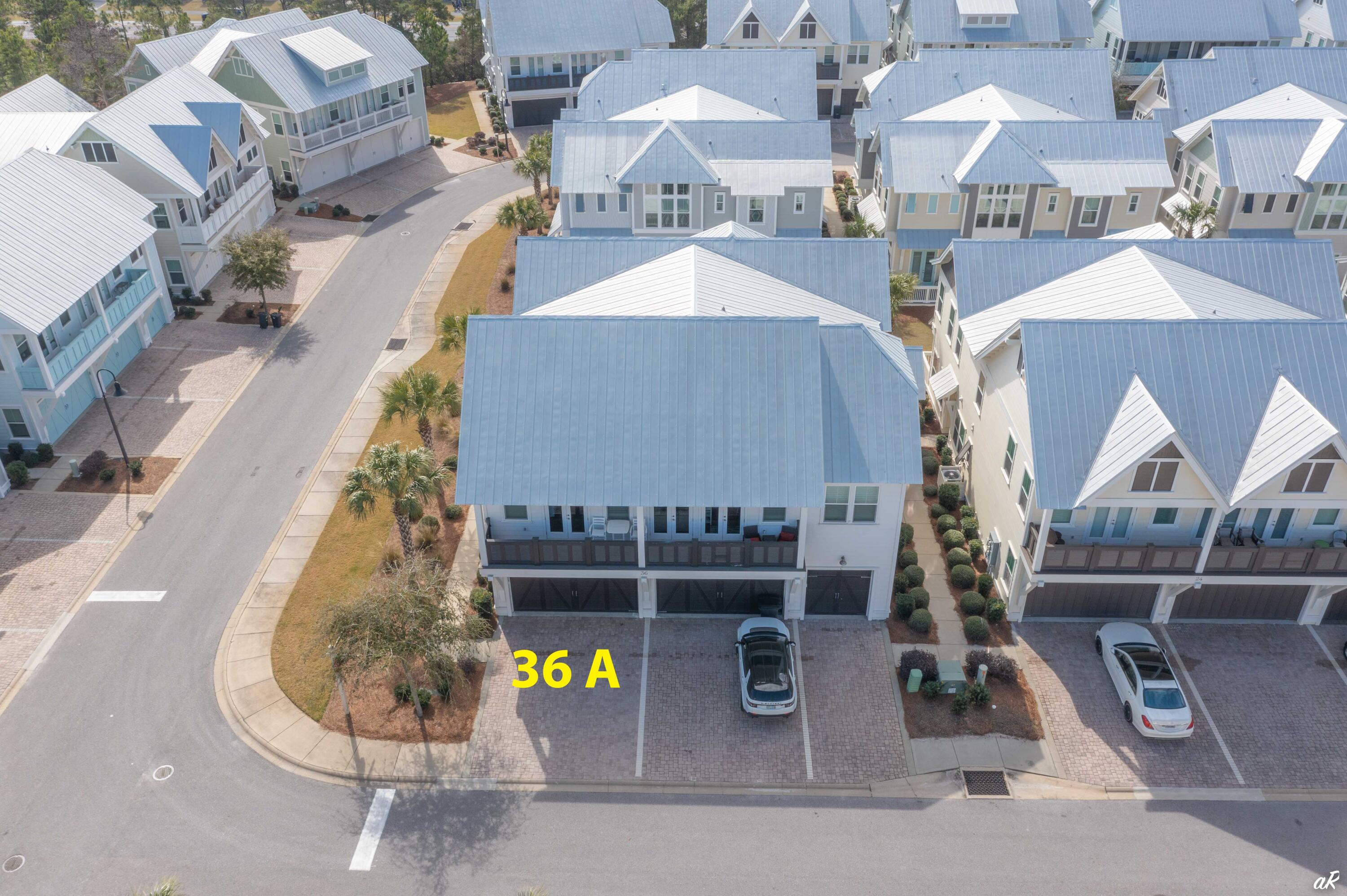 Aerial view of the blue-gray home marked 36 A, with a balcony, garages, and paved parking.