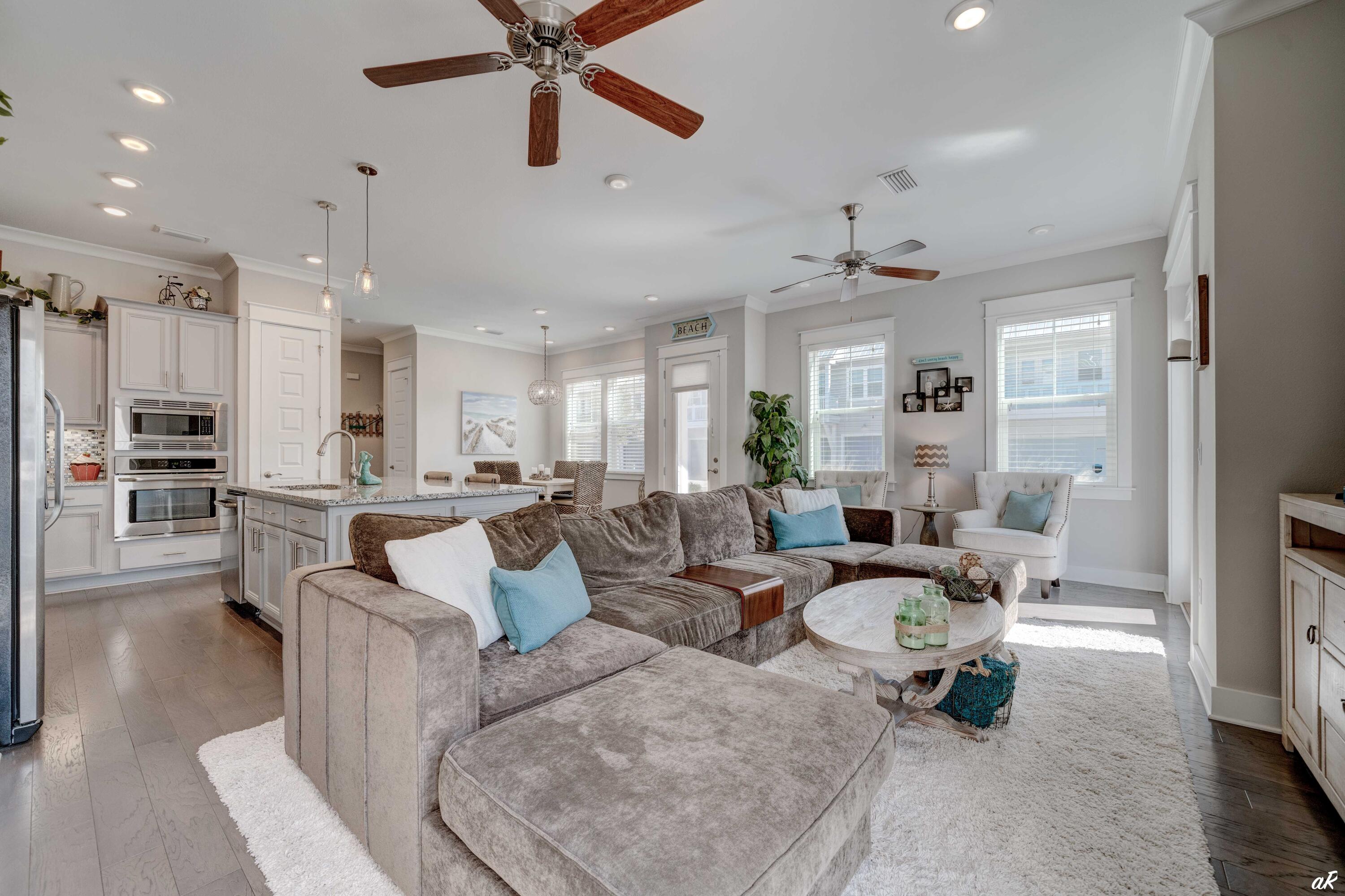 Open-plan living room with a large sectional, white kitchen island, and bright windows.