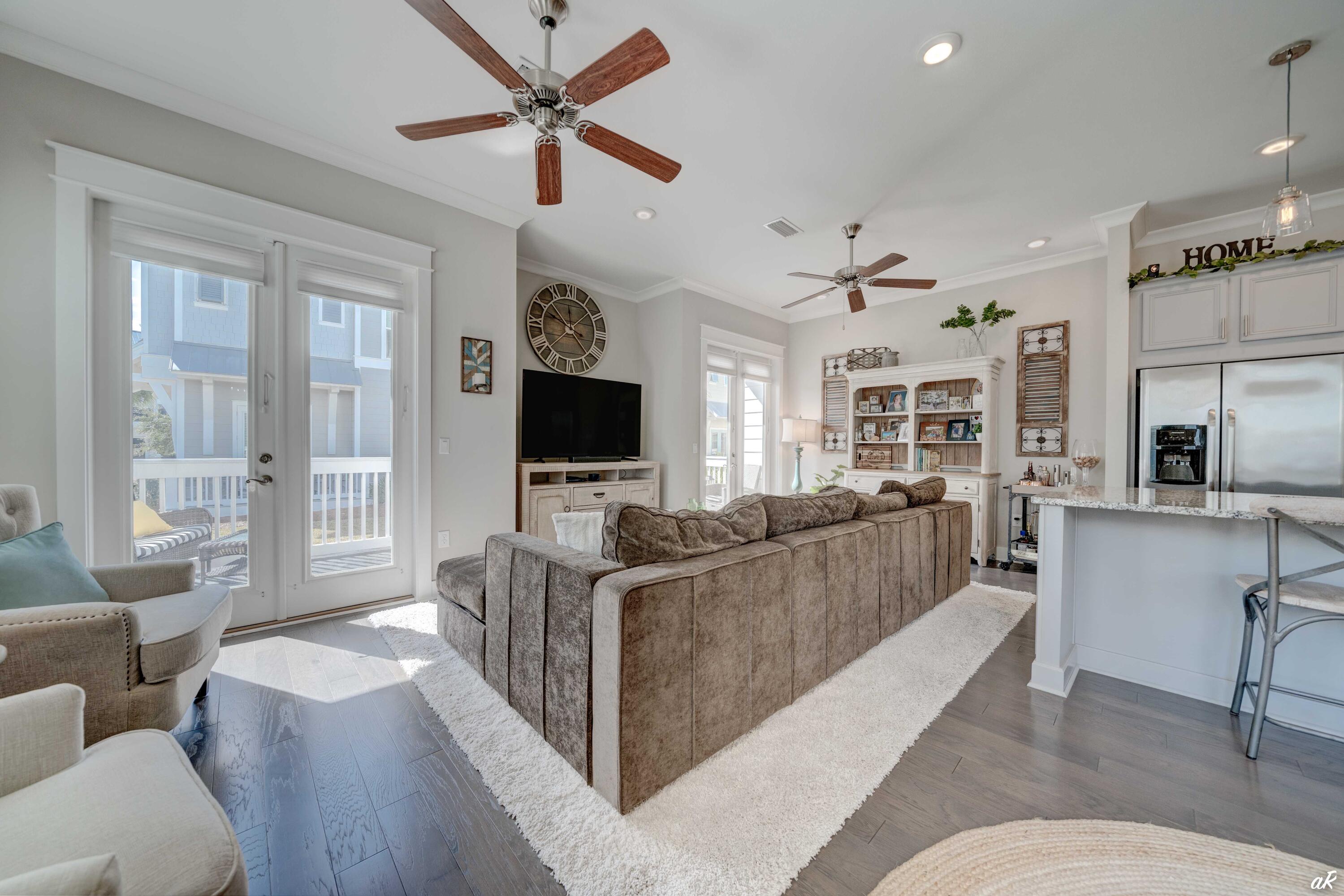 Open-plan living room with a large brown sectional, white rug, balcony doors, and adjoining kitchen.