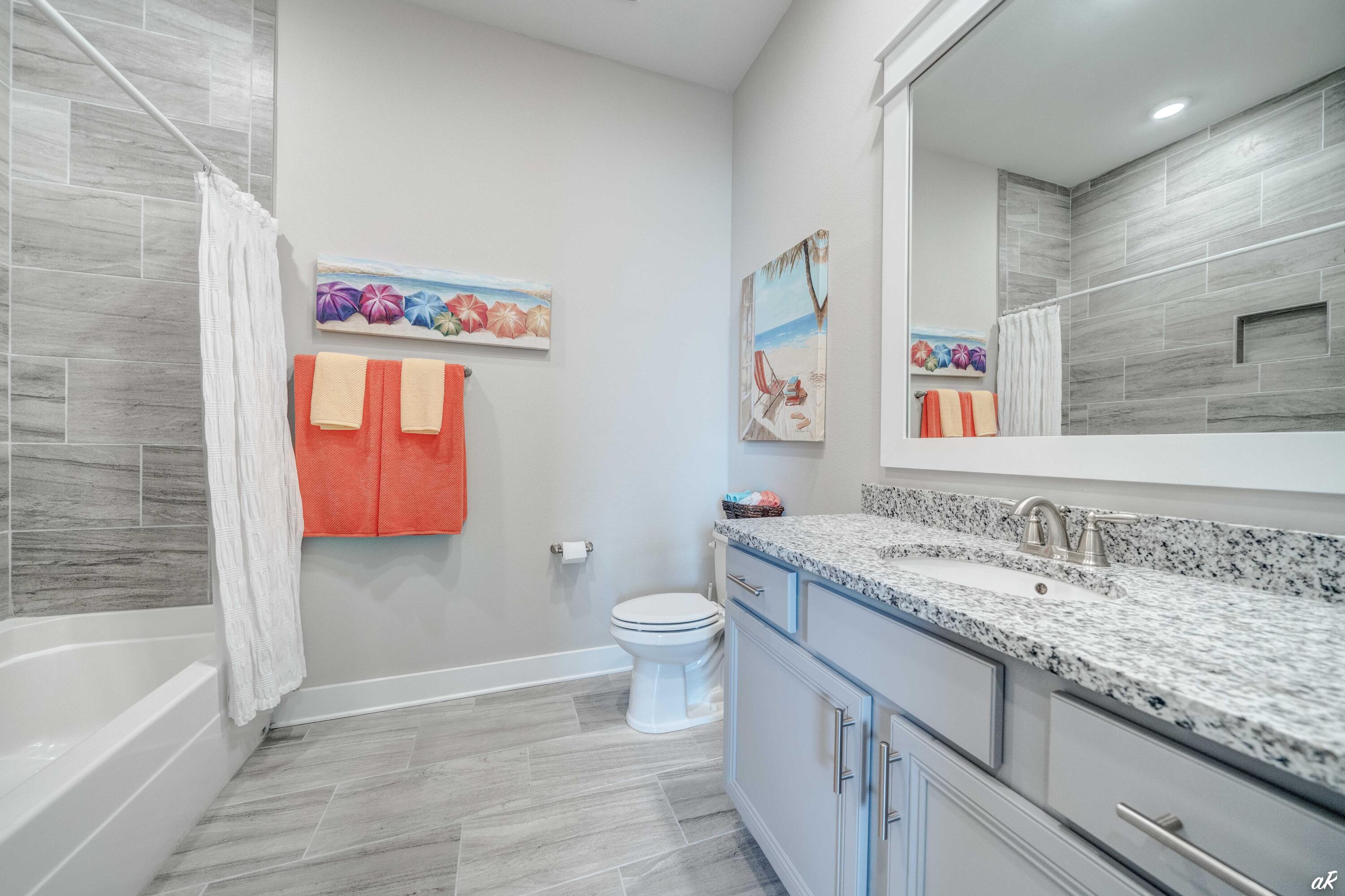 Bathroom with gray tile, a granite vanity, pale blue cabinets, and coral towels.