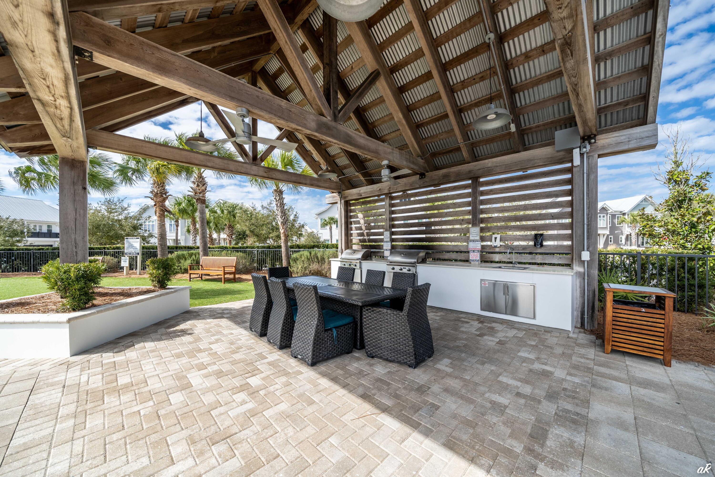 Covered patio with wicker dining set, two stainless steel grills, and palm trees beyond the railing.
