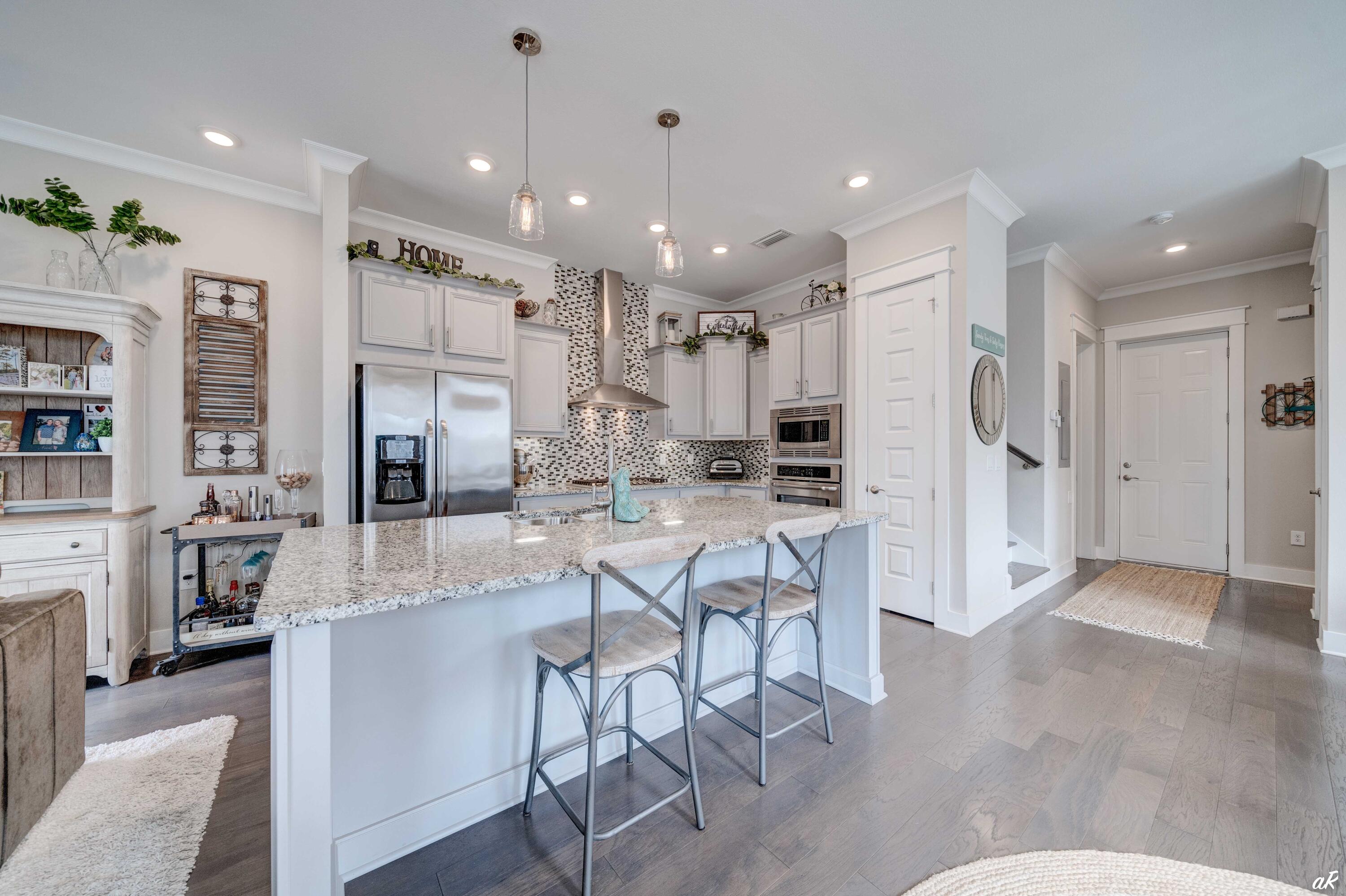 Kitchen with a granite island and two bar stools, white cabinets, stainless steel appliances, and a mosaic tile backsplash.