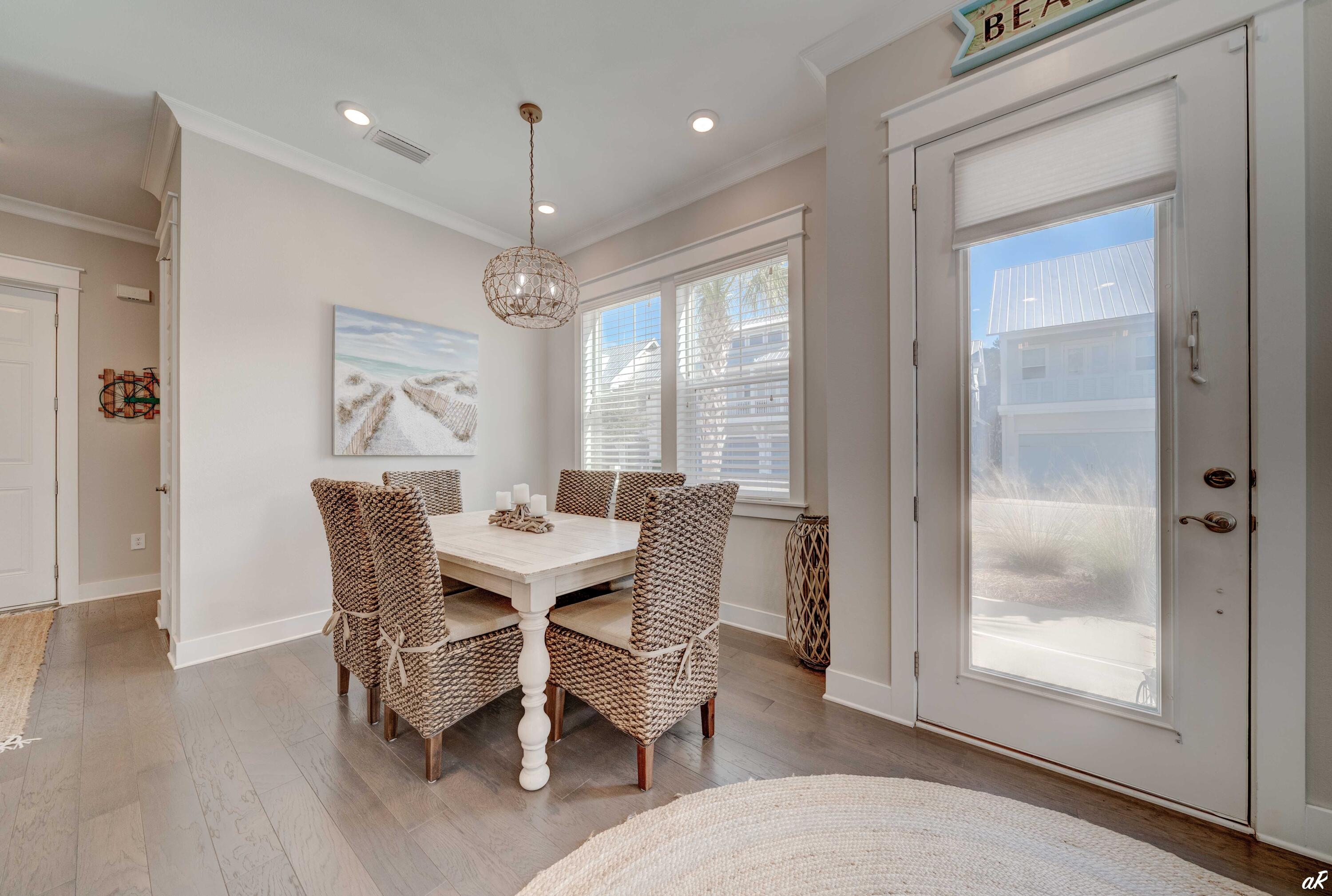 Dining area with a white table, woven chairs, beach-themed art, and a glass-paneled entry door.