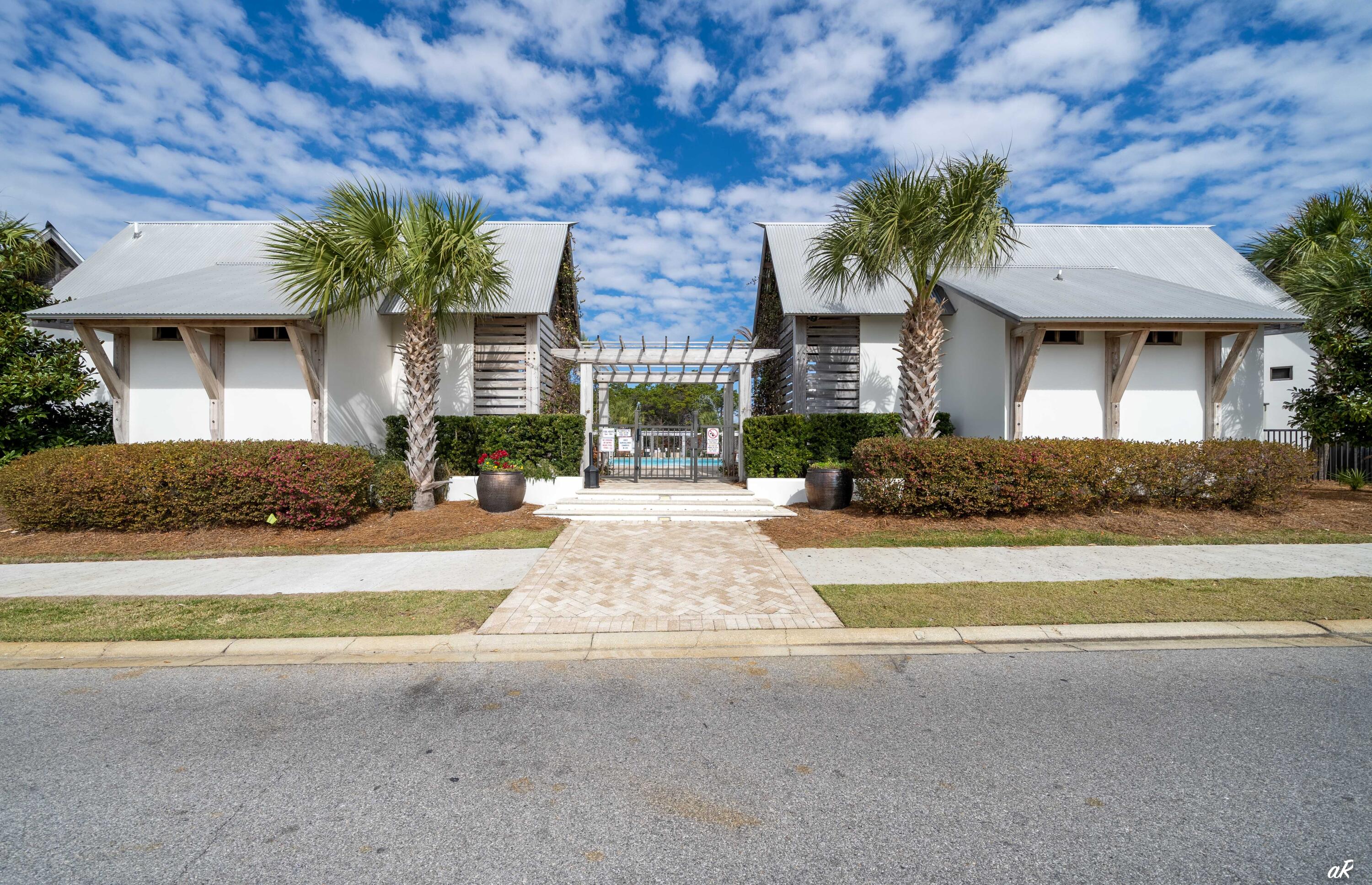 White coastal-style property with metal roofs, palm trees, and a gated entrance.