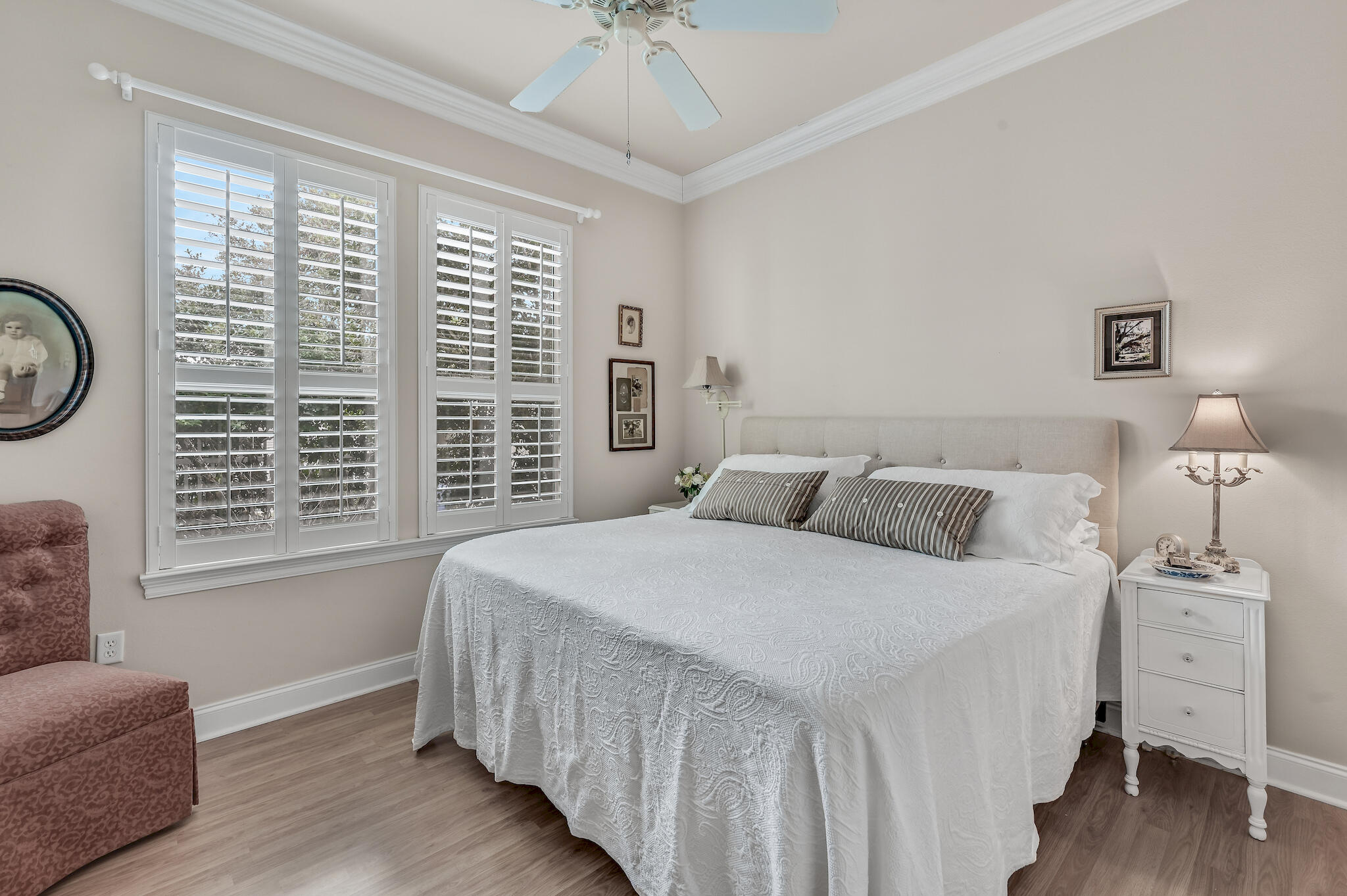 Bedroom with a white covered bed beside plantation-shuttered windows and a white bedside table.