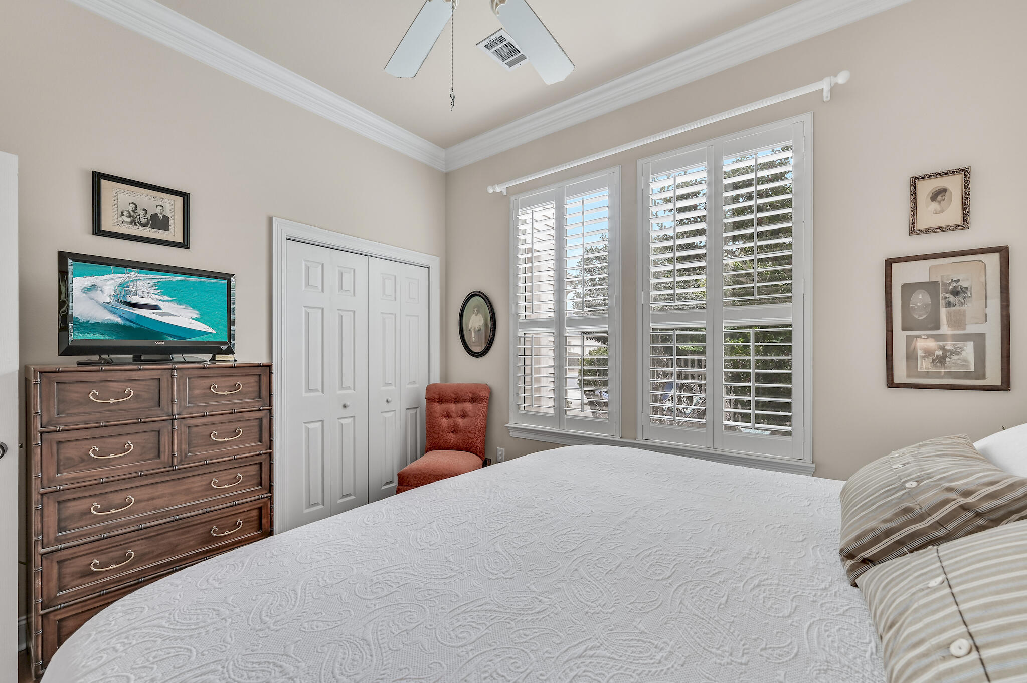 Bedroom with plantation-shuttered windows, a wooden dresser, and a red accent chair.