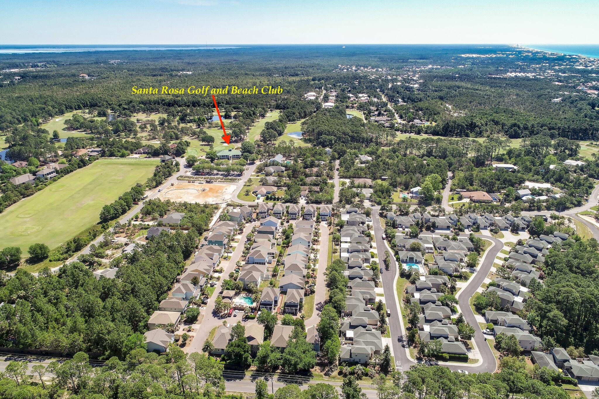 Aerial neighborhood view with the golf course and coastline in the distance.