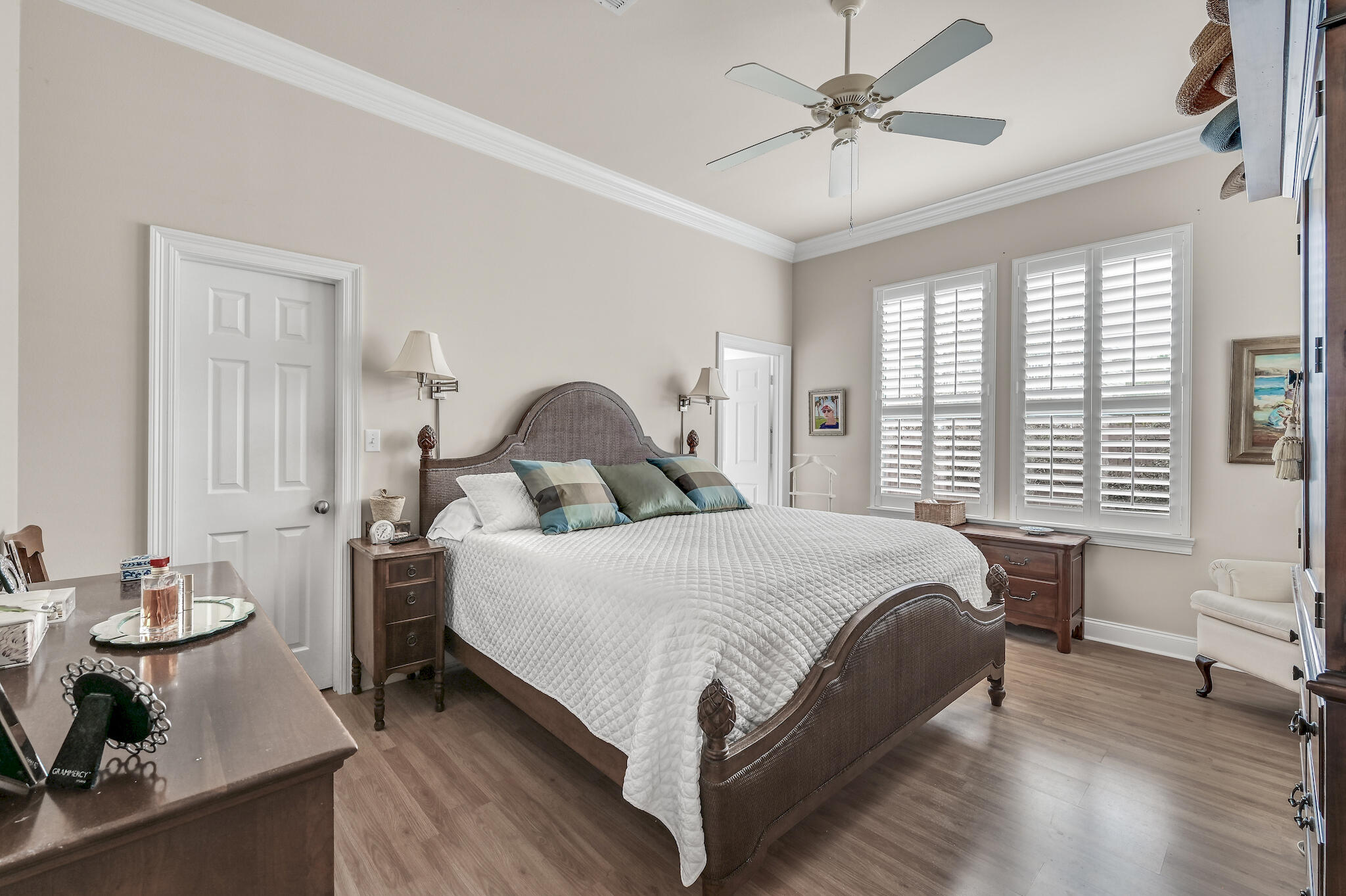 Furnished bedroom with a dark wood bed, white quilt, and tall windows with plantation shutters.