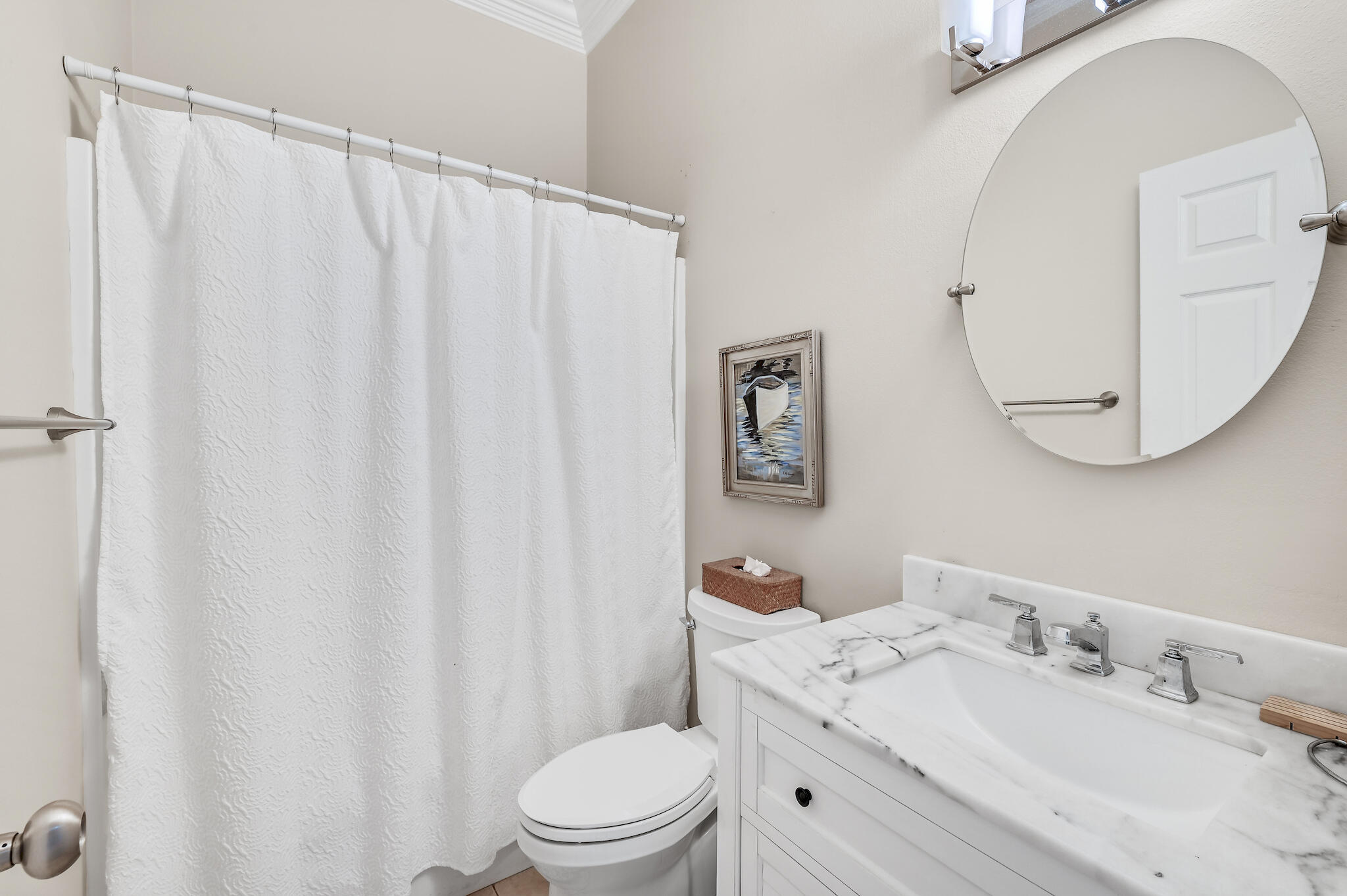 Bathroom with a marble-look vanity, large round mirror, and white shower curtain.