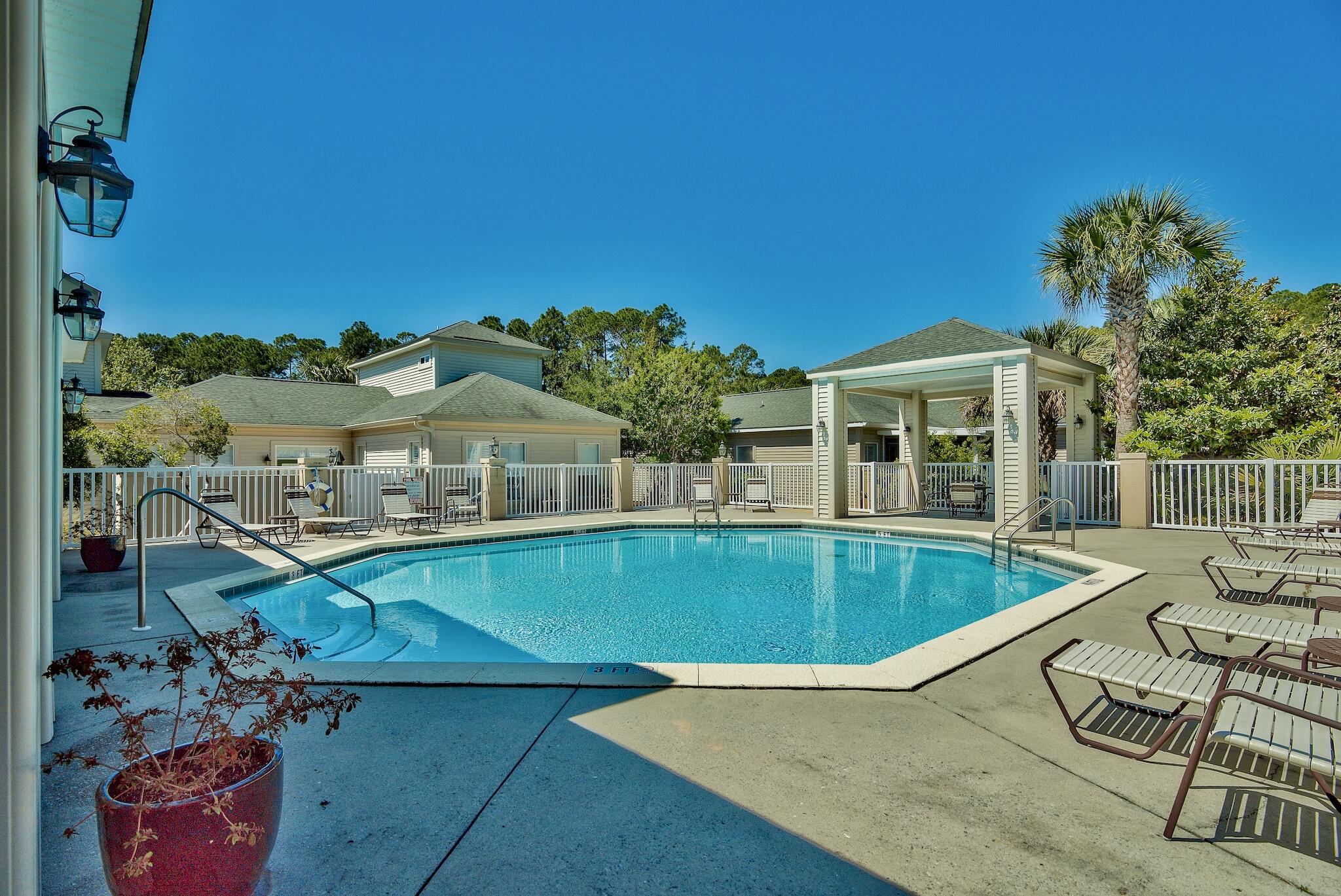 Outdoor swimming pool with lounge chairs, a covered pavilion, and palm trees.