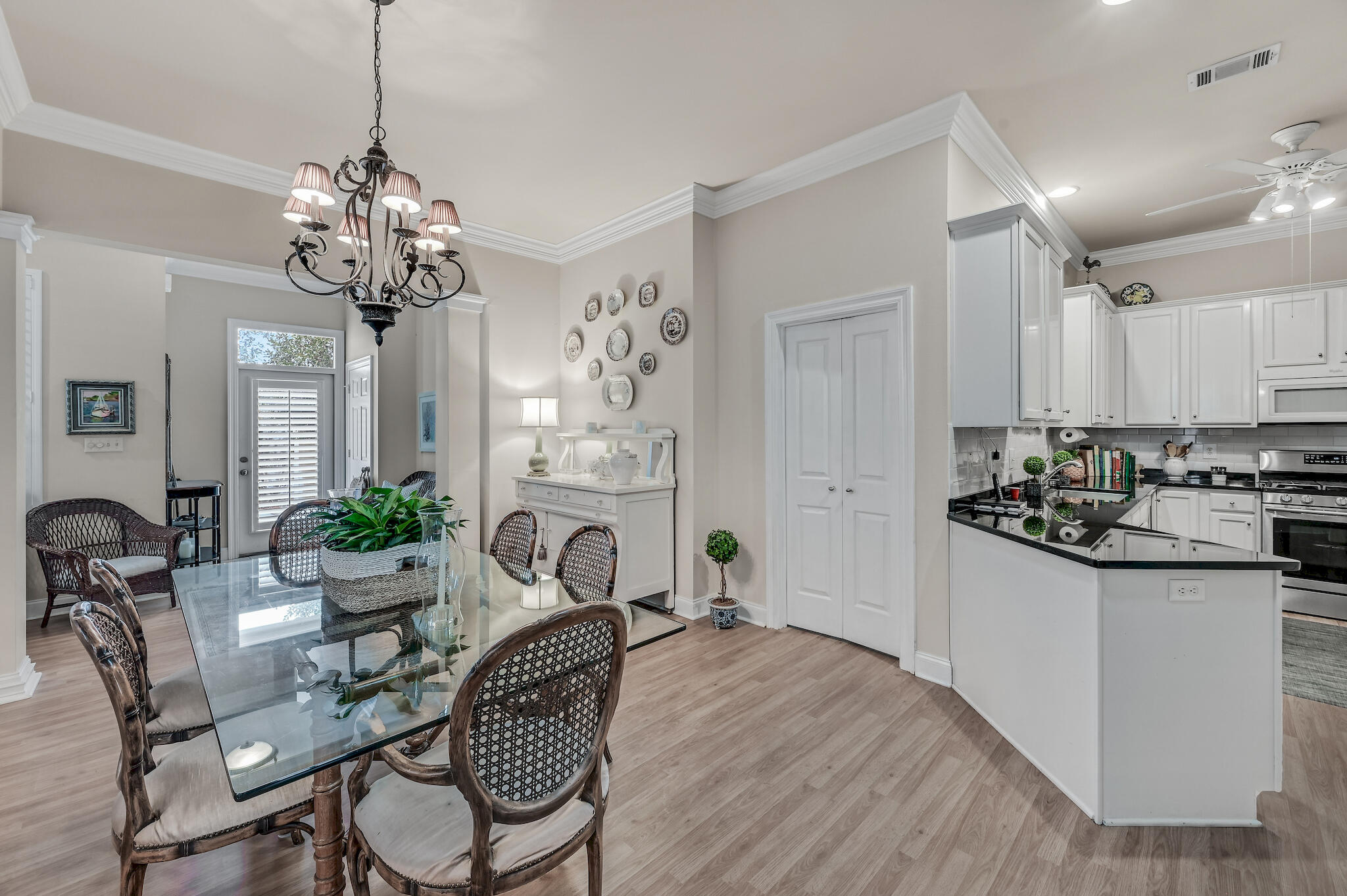 Dining area with glass table and woven chairs beside a white kitchen with black countertops.