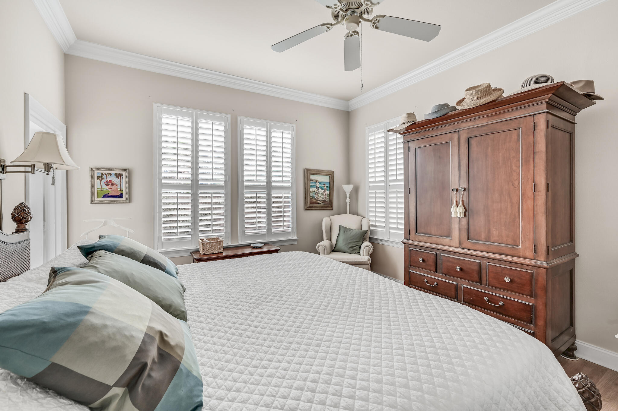 Bedroom with plantation shutters, a large wooden armoire, and a white quilted bed.