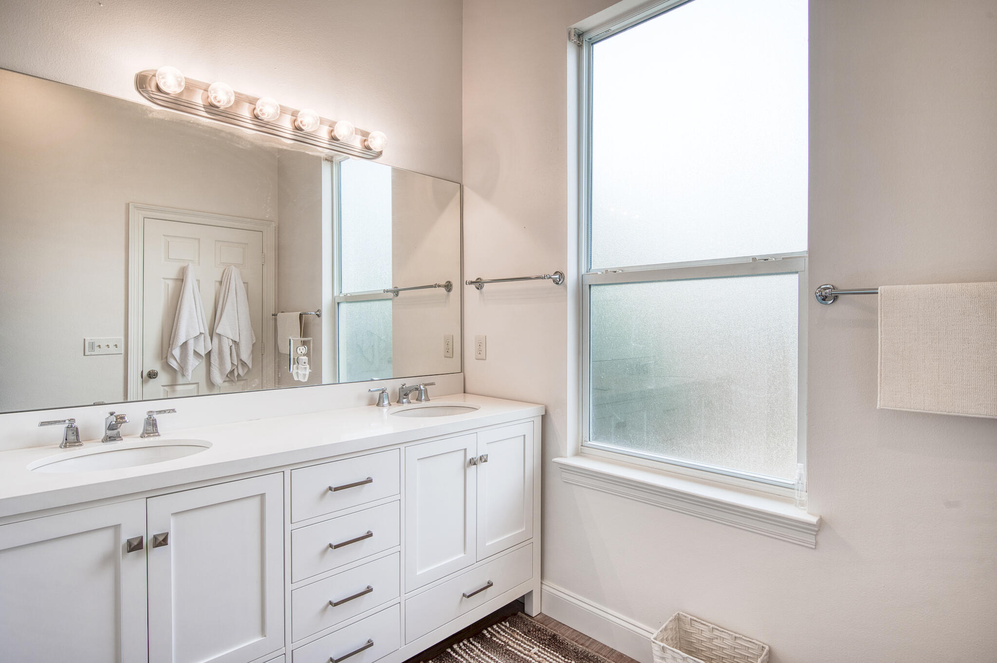 Bathroom with a white double-sink vanity, large mirror, and tall frosted window.