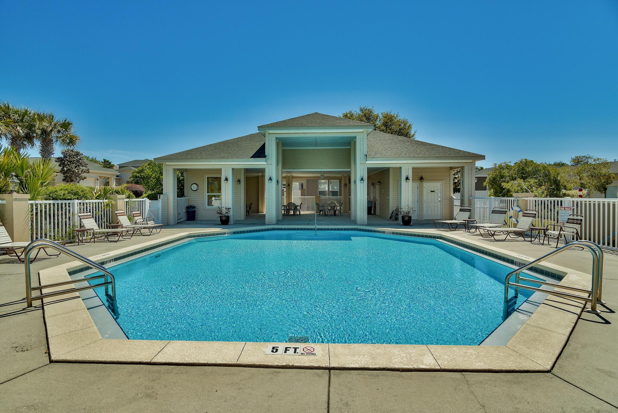 Outdoor swimming pool and covered pavilion with seating, lounge chairs, and a fenced deck.