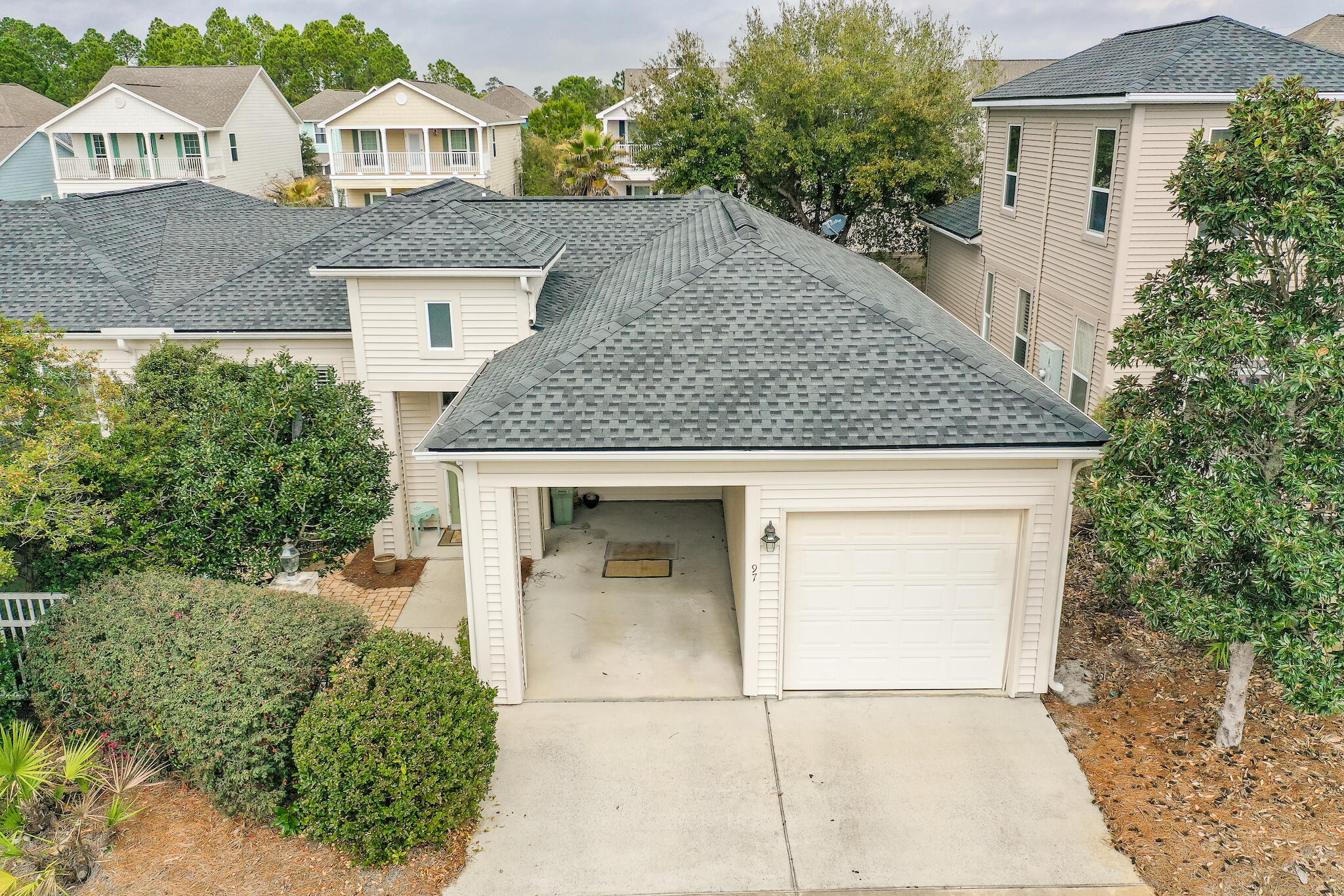 Aerial view of a cream-colored home with gray roofs, an open garage, and a wide driveway.