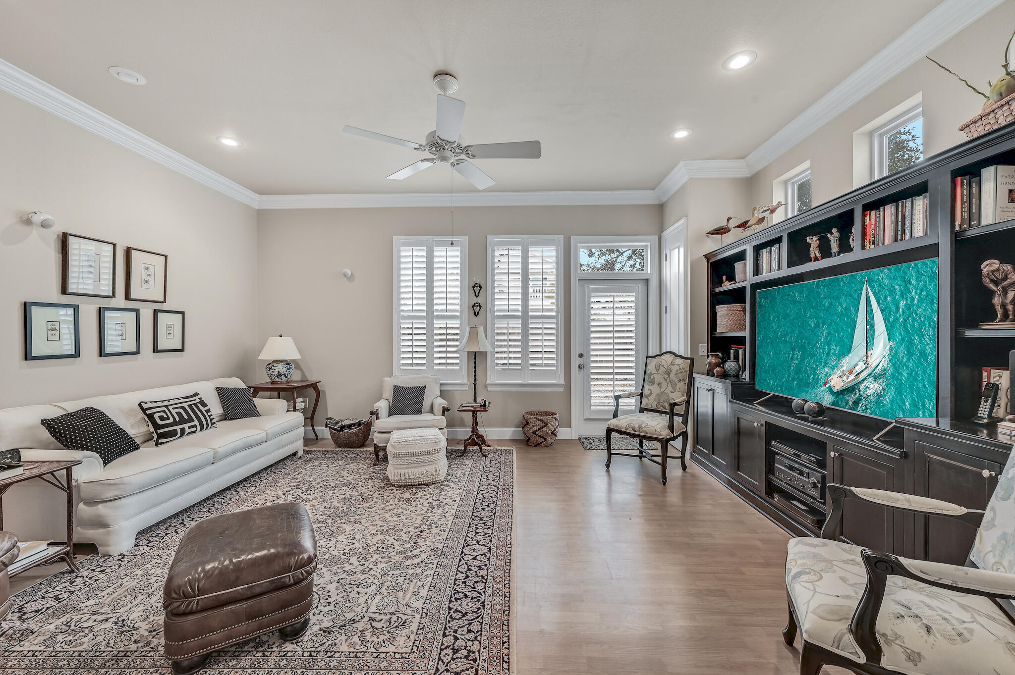 Living room with a white sofa, patterned rug, plantation shutters, and dark built-in entertainment center.