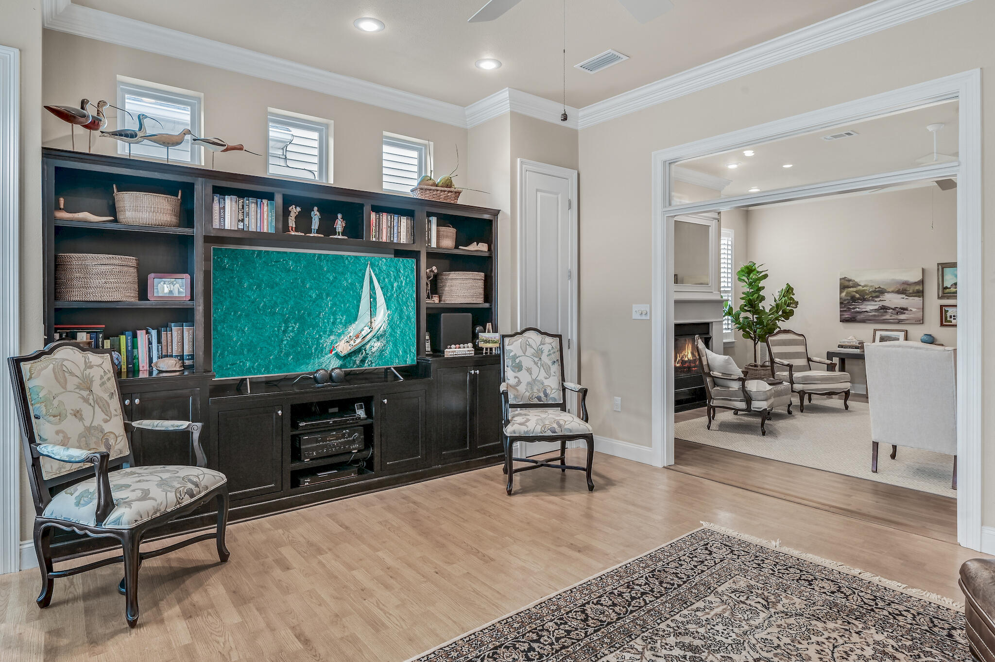 Media room with a television in dark built-in bookcases, upholstered chairs, and a doorway to a fireplace sitting room.