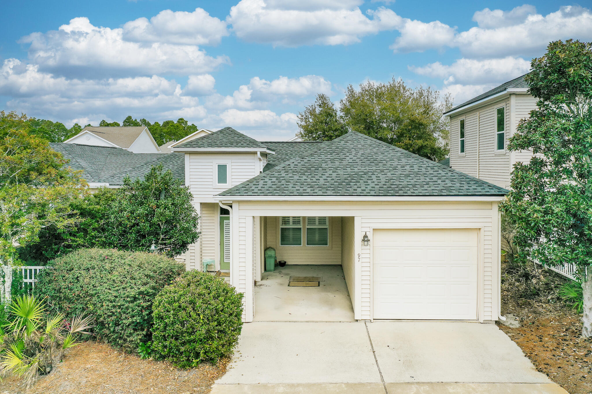 White-sided home with a green shingle roof, attached garage, open covered parking bay, and landscaped yard.