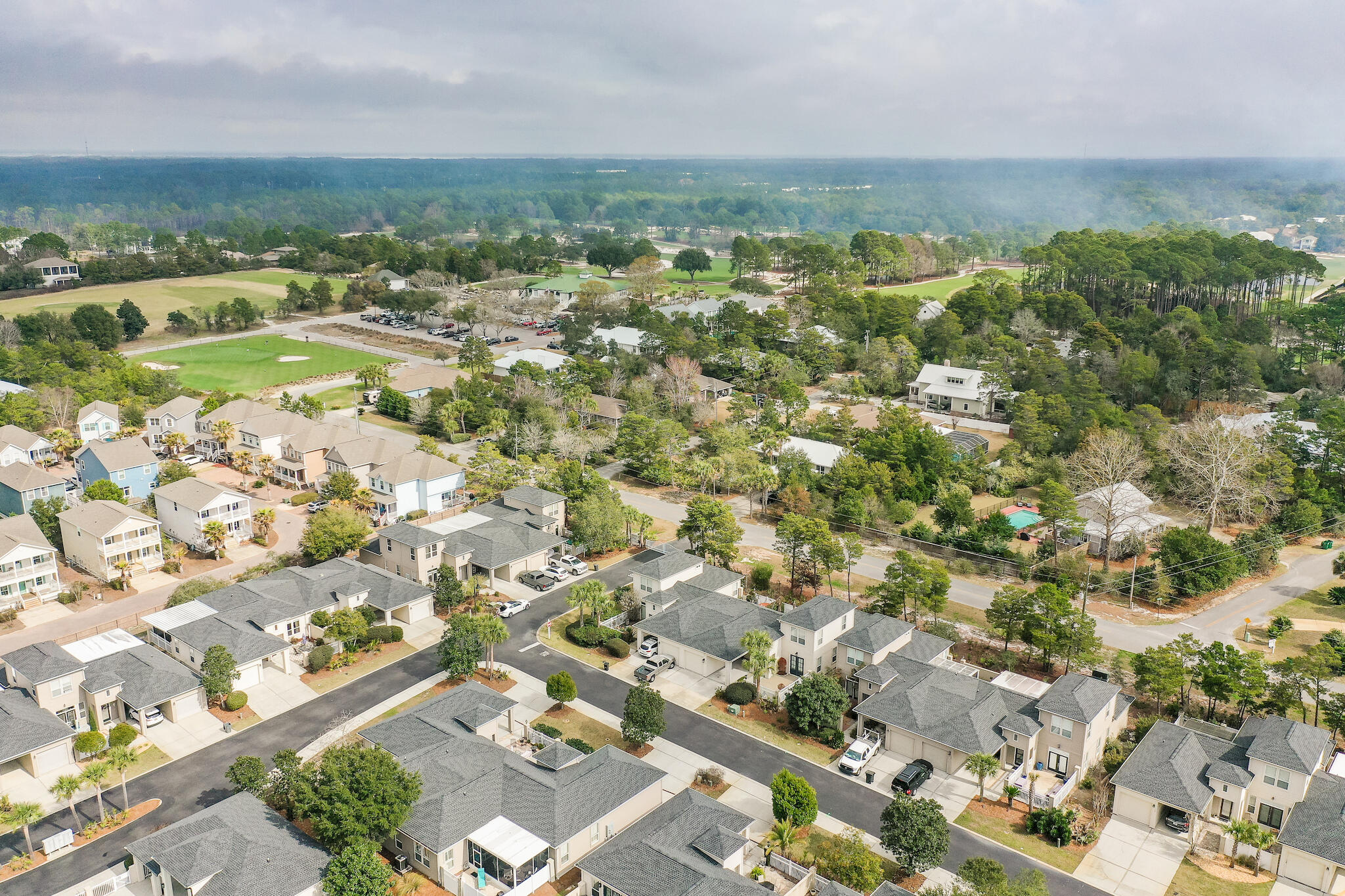 Aerial view of a residential neighborhood beside a golf course and wooded areas.