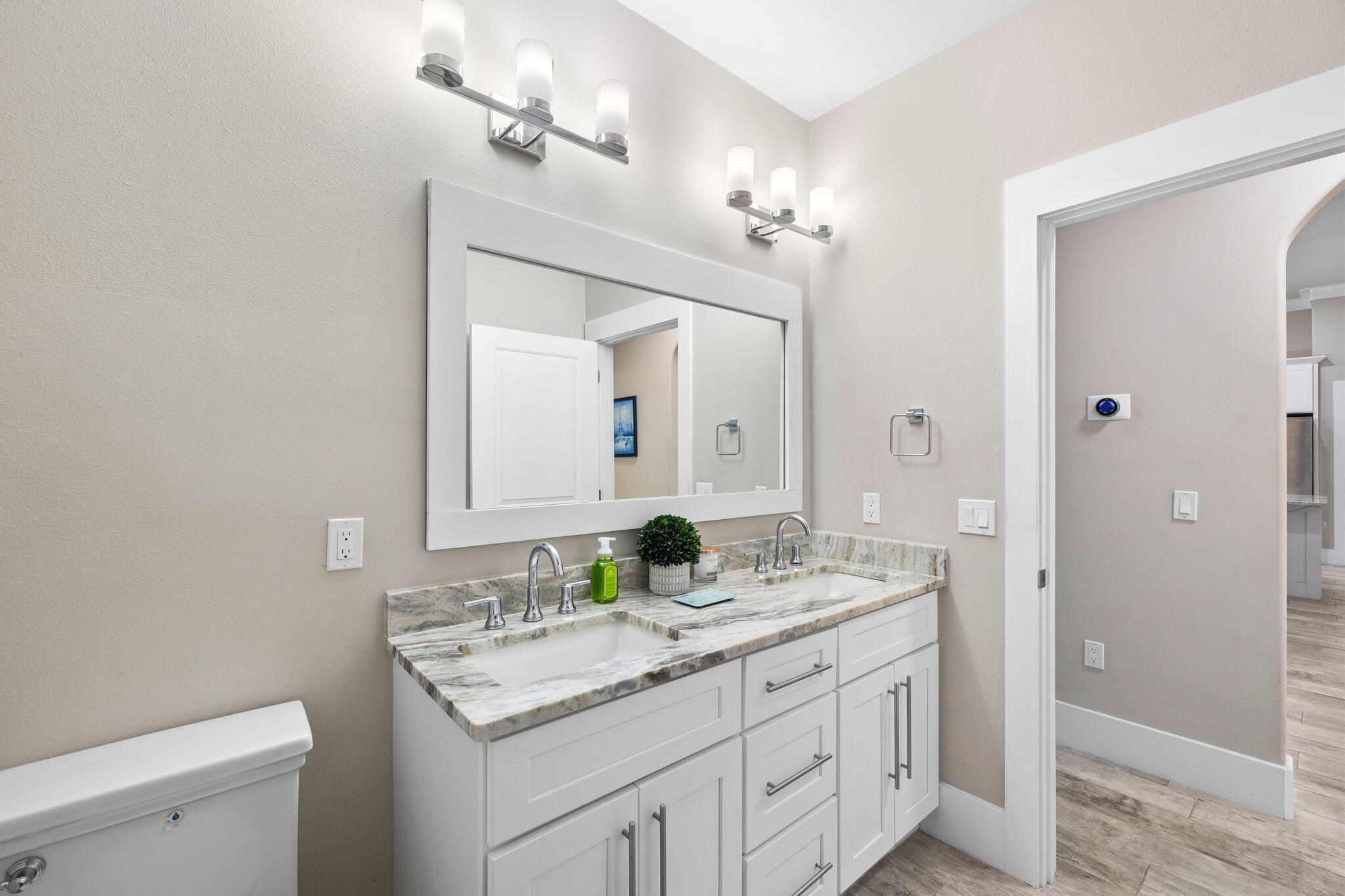 Bathroom with a double-sink white vanity, veined stone counter, and large framed mirror.