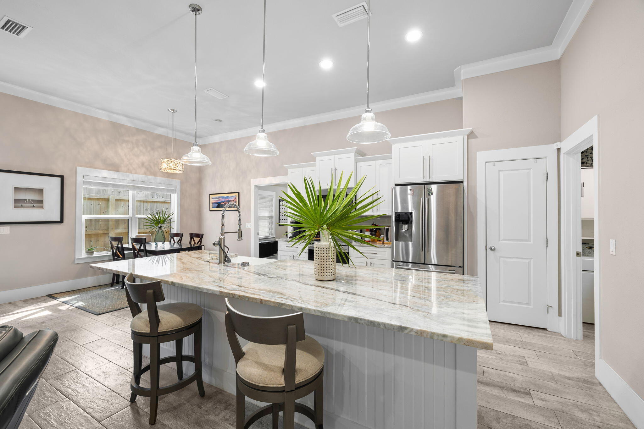 Kitchen with a large stone-topped island, bar stools, white cabinets, and stainless steel refrigerator.