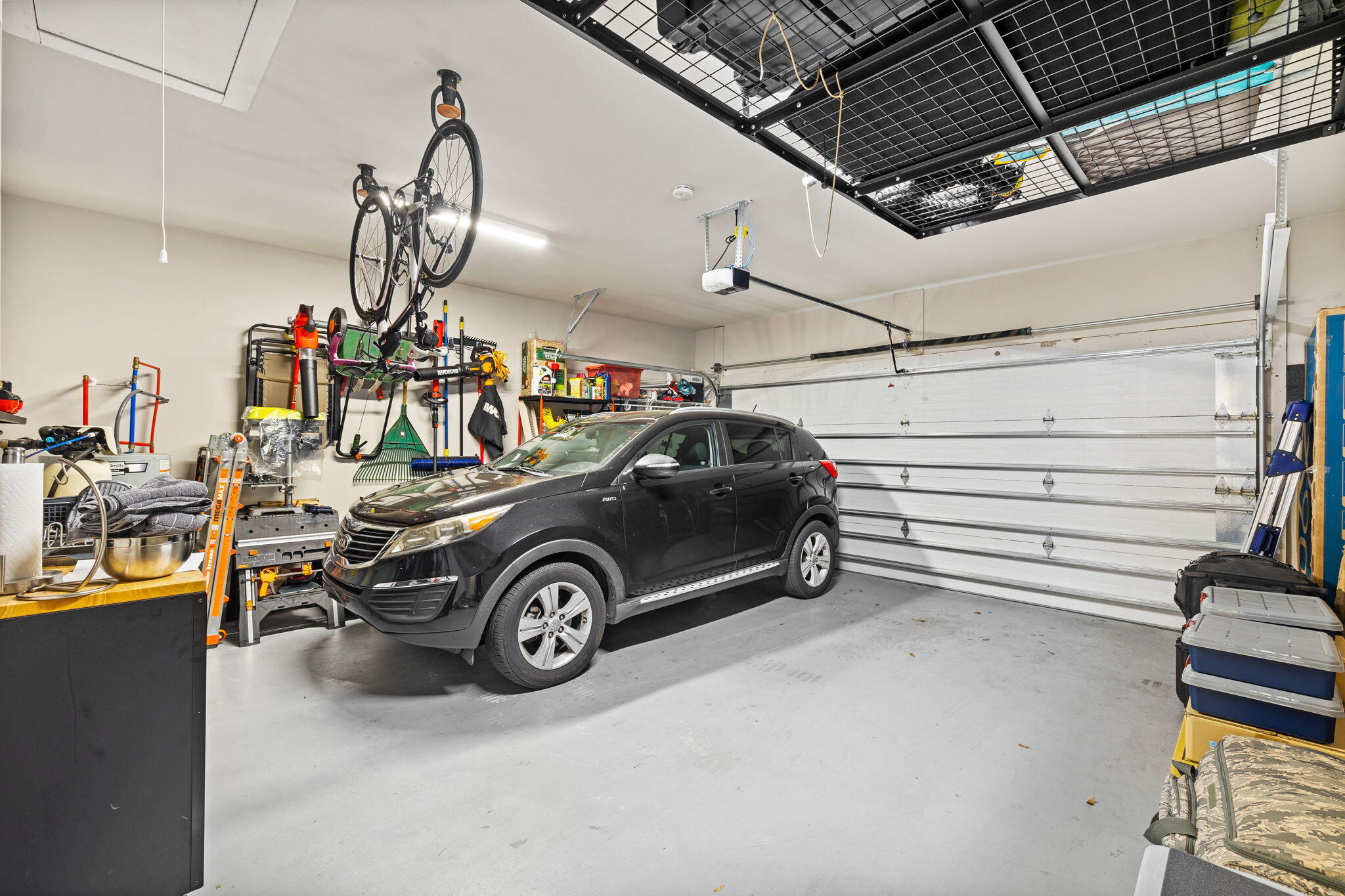 Garage with a black SUV, wall-mounted tools, bicycles, and overhead storage racks.