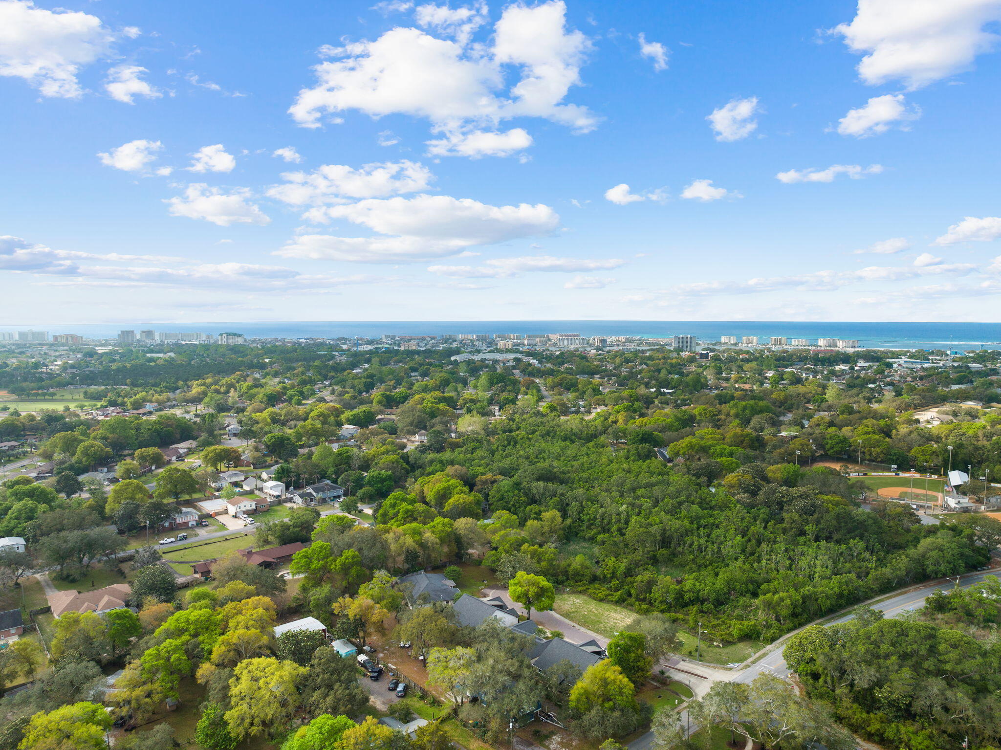 Aerial view of a leafy Destin neighborhood, with the Gulf and coastal skyline in the distance.