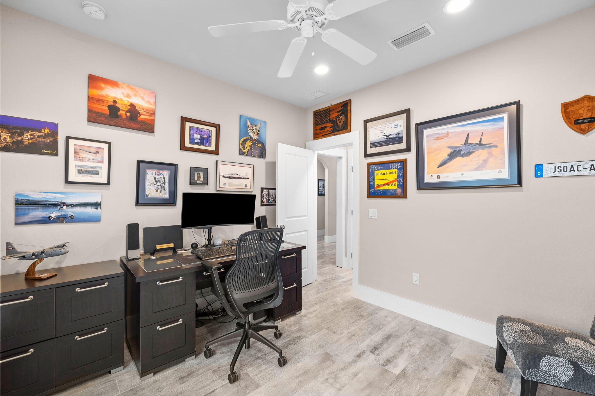 Home office with dark cabinetry, computer desk, mesh chair, and aviation memorabilia on the walls.