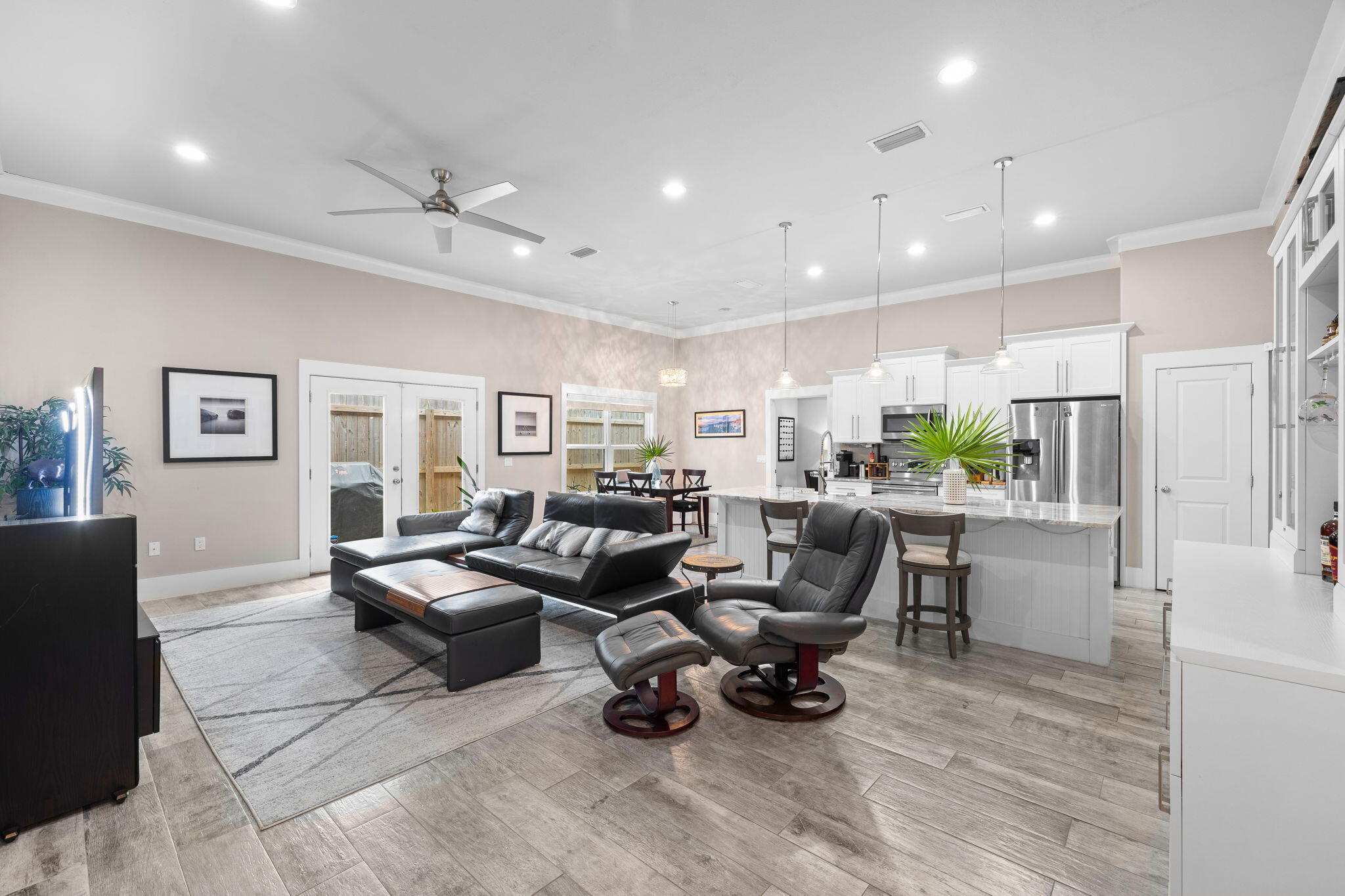 Open-plan living room and kitchen with black leather seating, a white island, and stainless steel appliances.