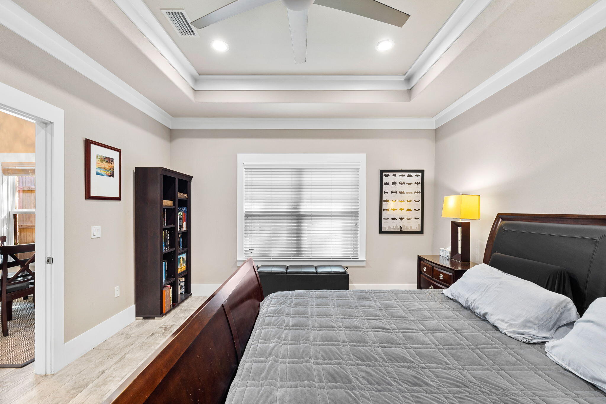 Furnished bedroom with a gray quilted bed, dark wood furniture, and a tall bookcase.
