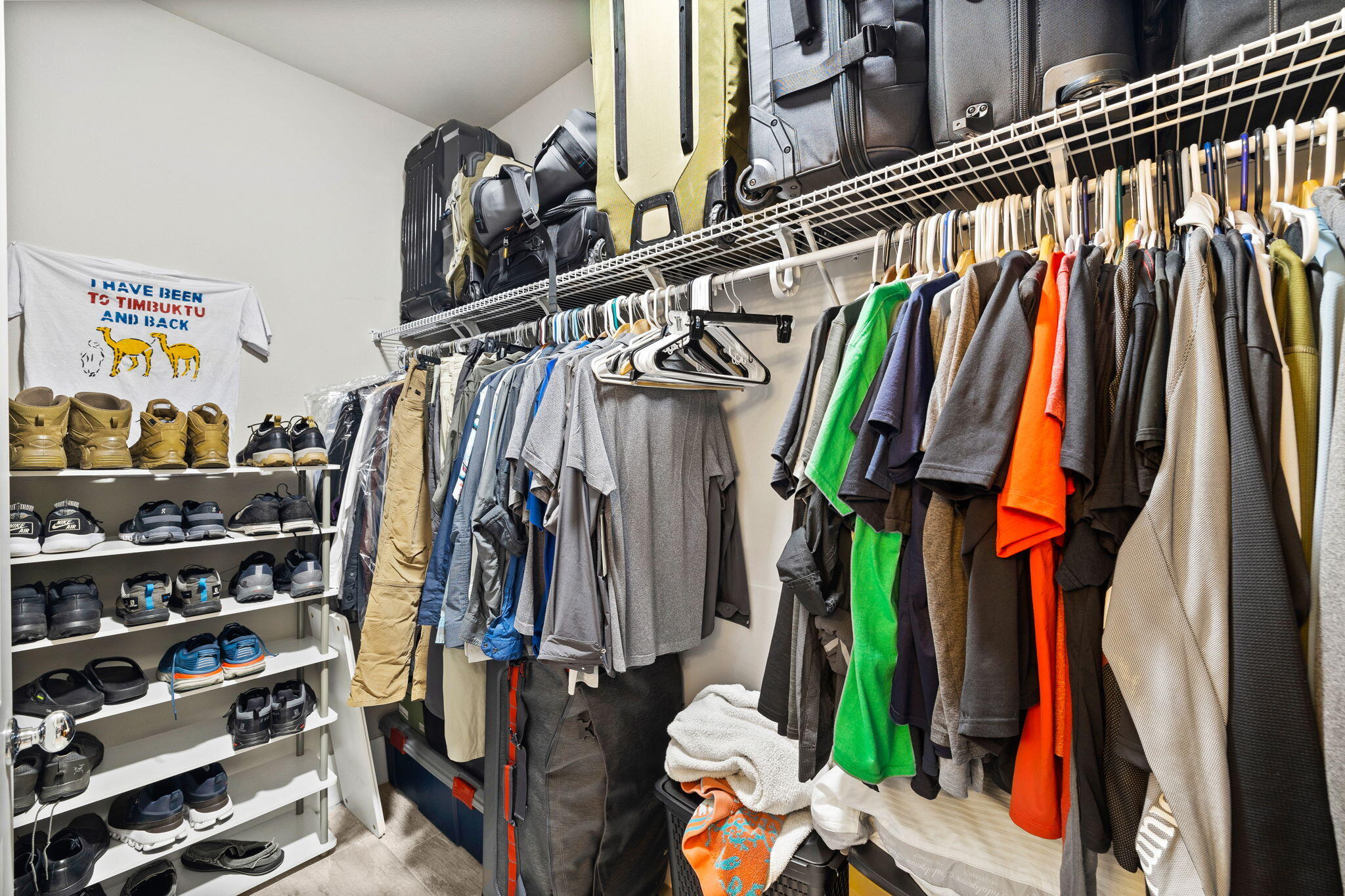 Walk-in closet with densely packed clothing, rows of shoes, and luggage on upper shelves.