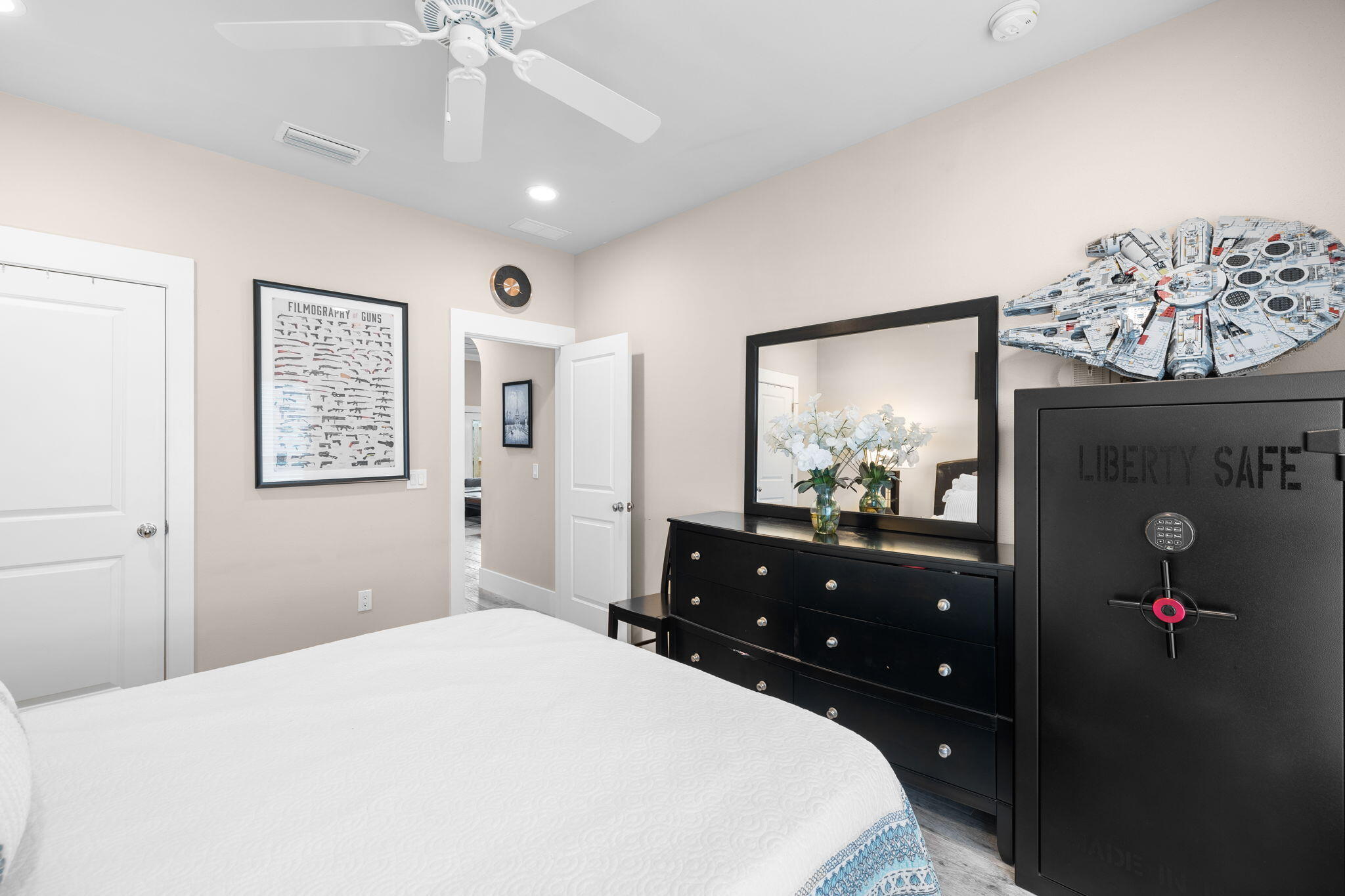 Bedroom with a white bed, black dresser, Millennium Falcon model, and large safe.