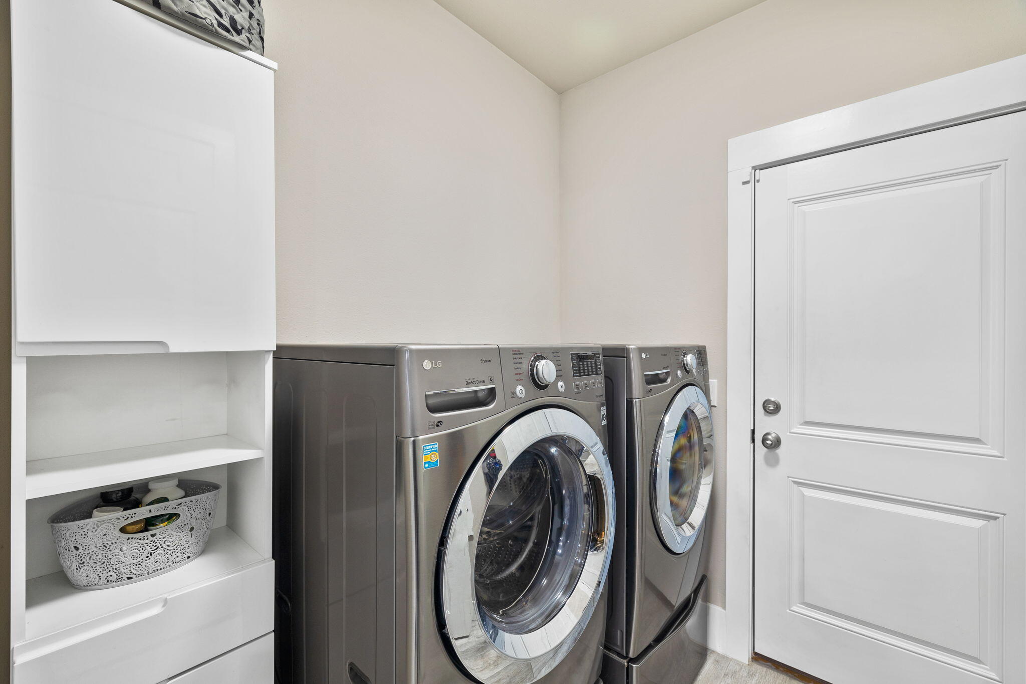 Laundry room with front-loading washer and dryer beside built-in white shelving.