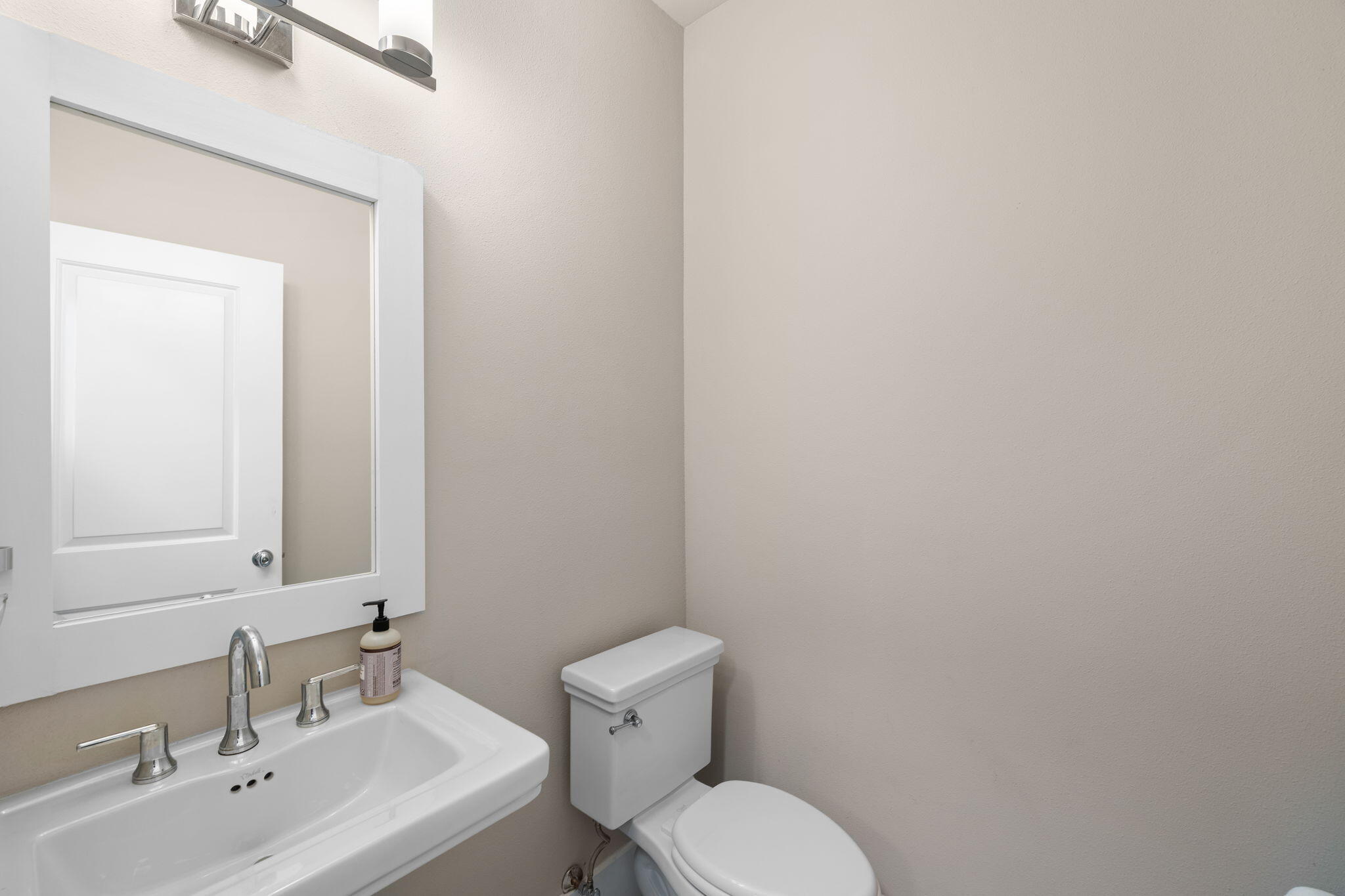 Bathroom with a white sink vanity, large mirror, chrome fixtures, and toilet.