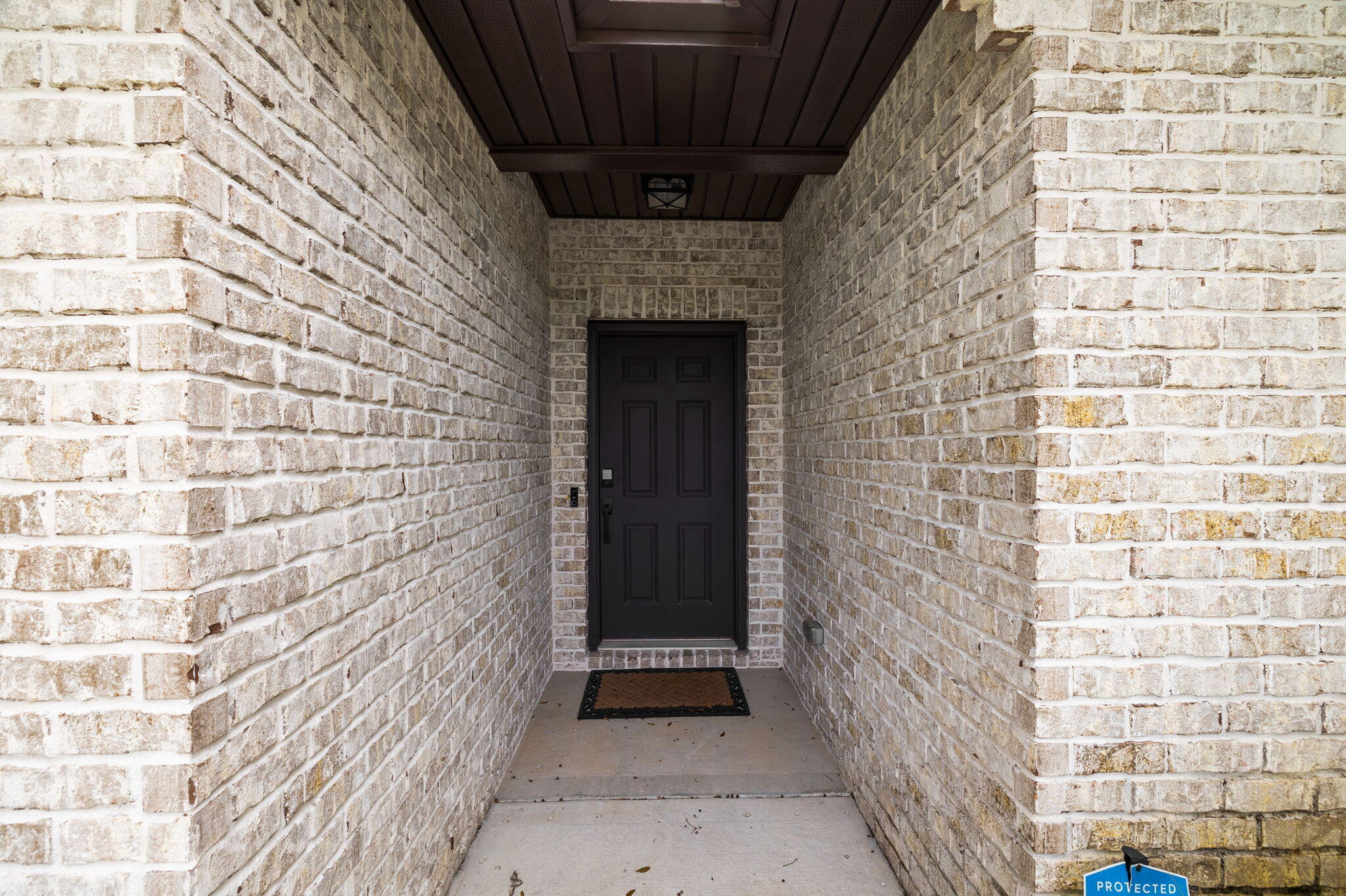 Recessed dark front door framed by light brick walls beneath a covered porch.