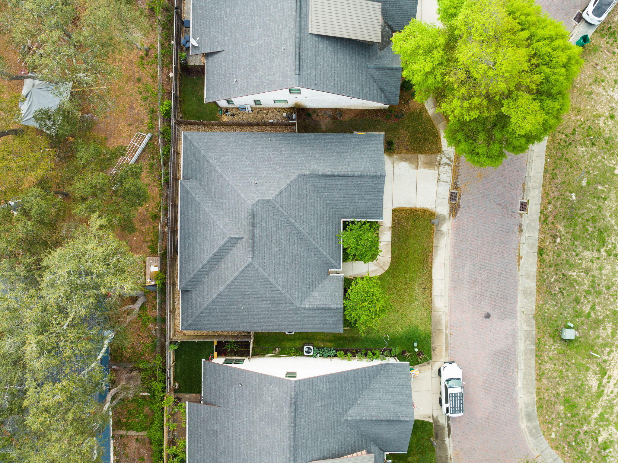 Aerial view of a gray-shingled home with a driveway, small lawn, and mature trees.