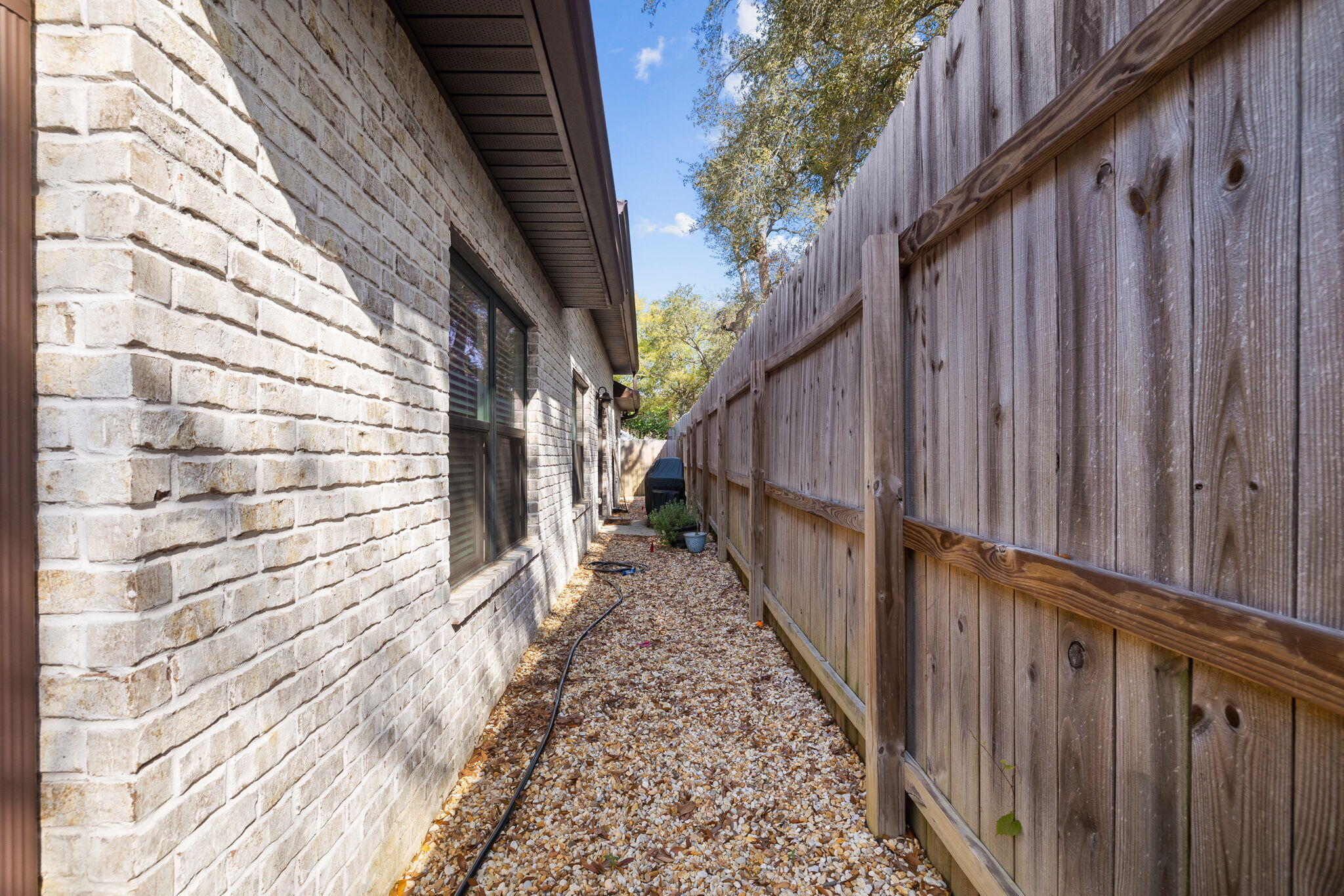 Side yard with a gravel path between a light brick house and a tall wooden privacy fence.