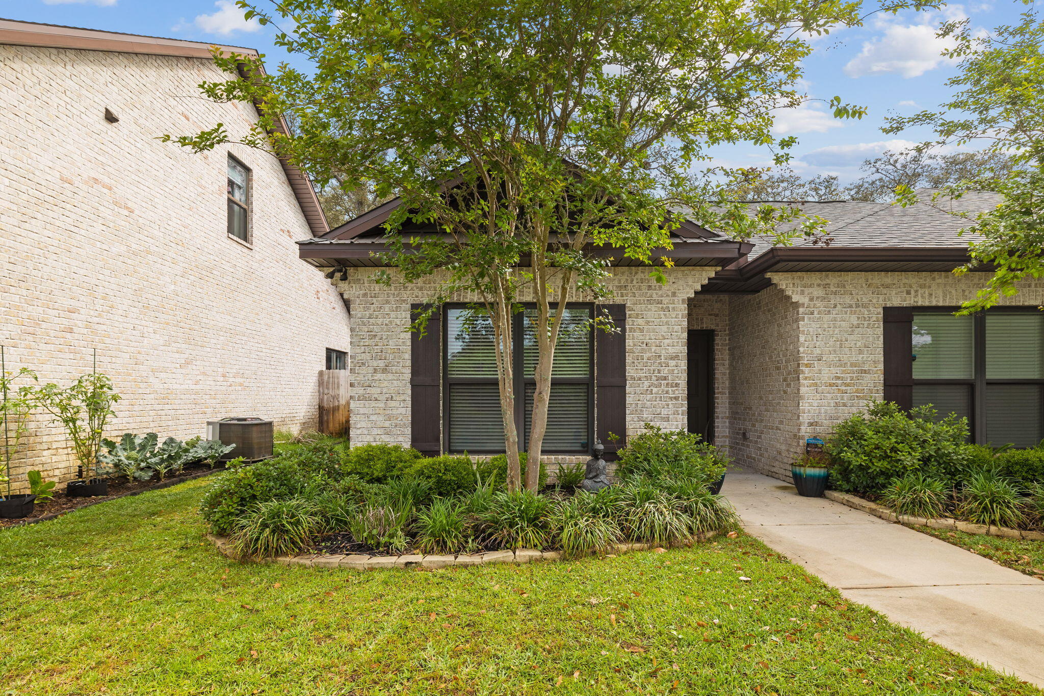 Light brick home with a recessed covered entry, mature tree, and landscaped garden beside a curved walkway.