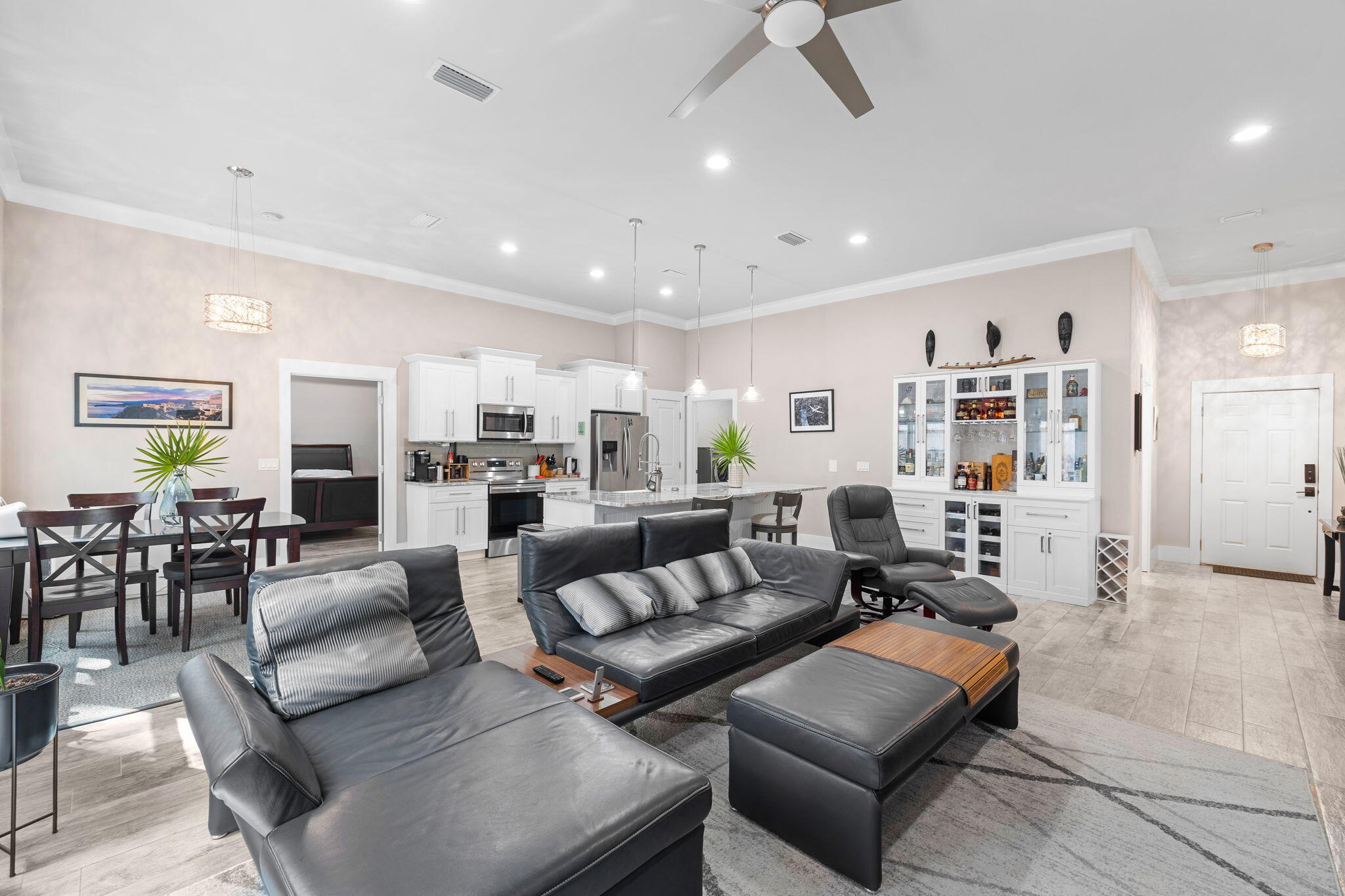 Open-plan living room with black leather sectional, dining area, and white kitchen with island.