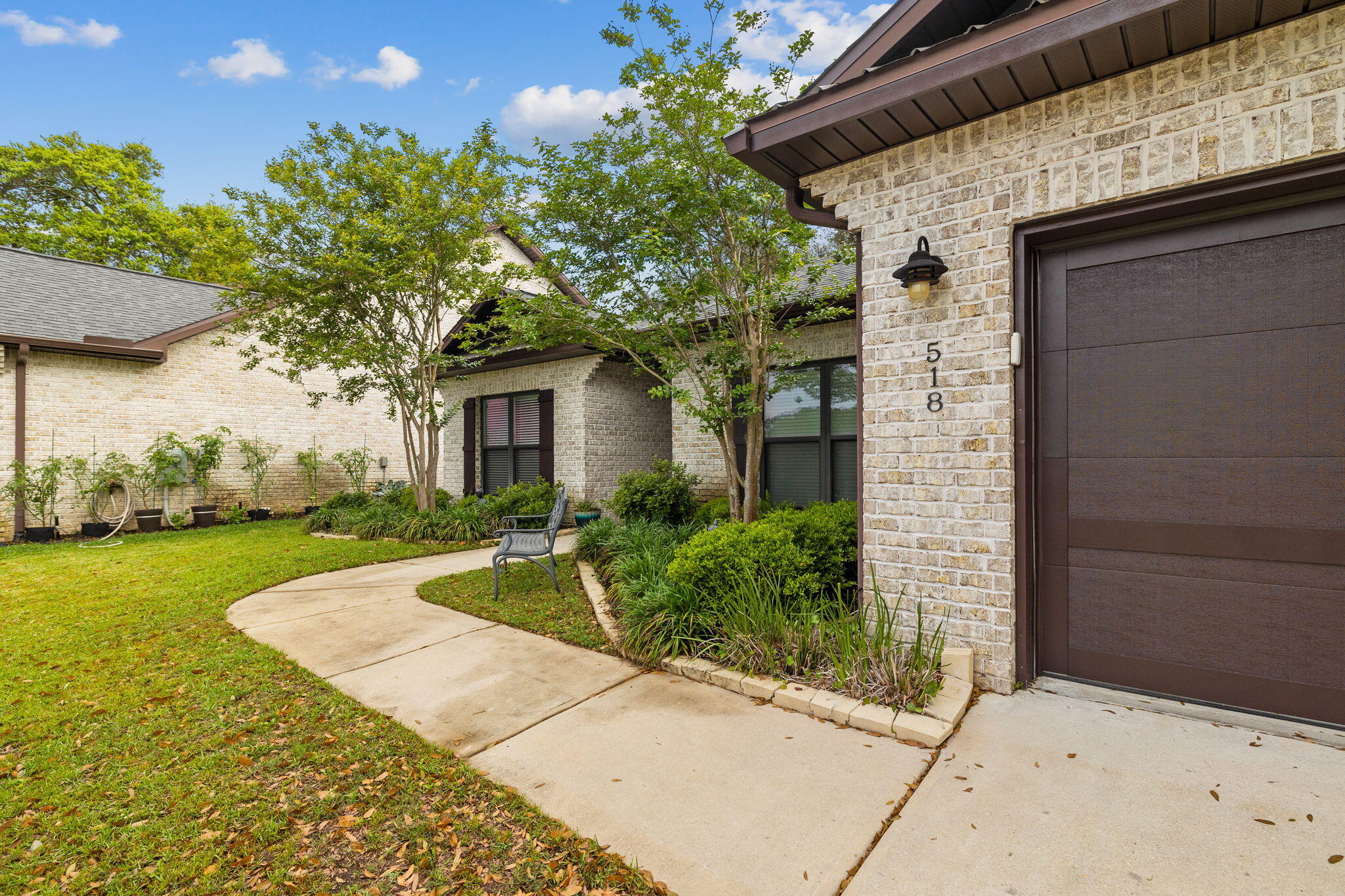 Light brick home exterior with dark garage door, landscaped walkway, and bench.