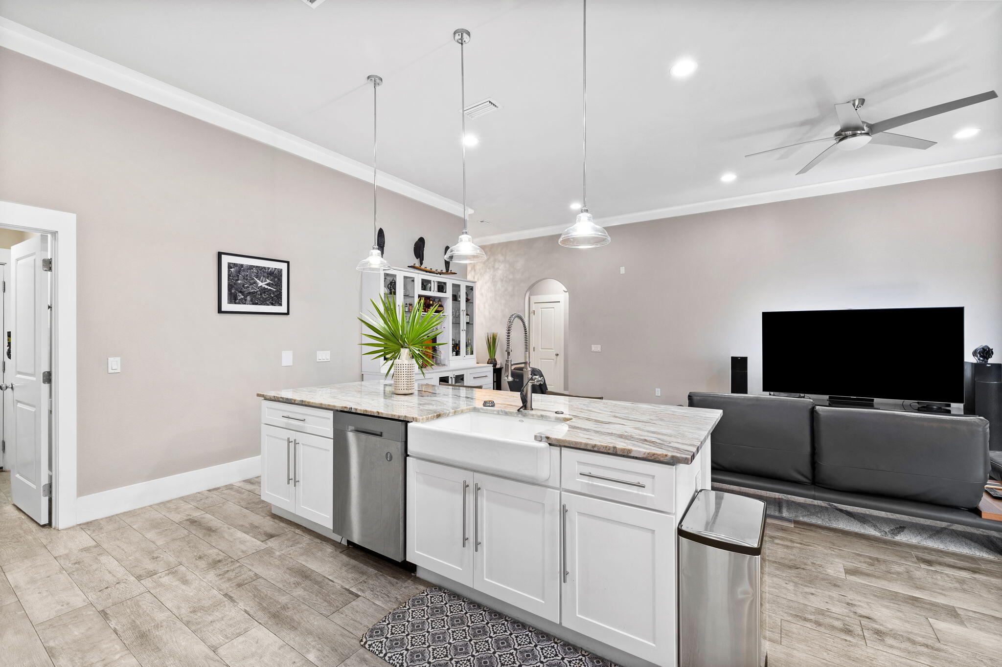Open-plan kitchen with a large white island and farmhouse sink beside a gray living-room sofa.