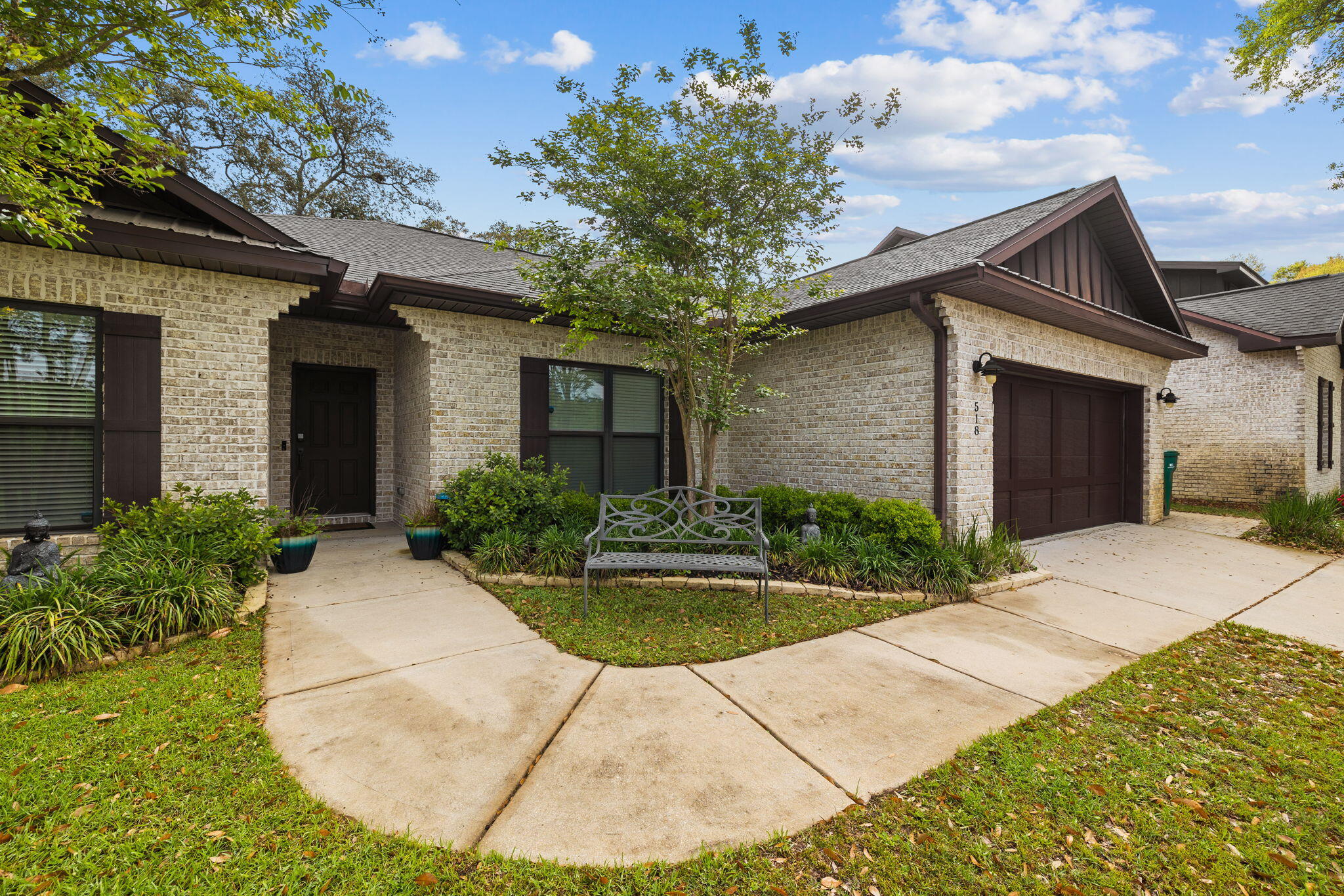 Brick home with dark brown trim, attached garage, and a curved walkway beside a garden bench.