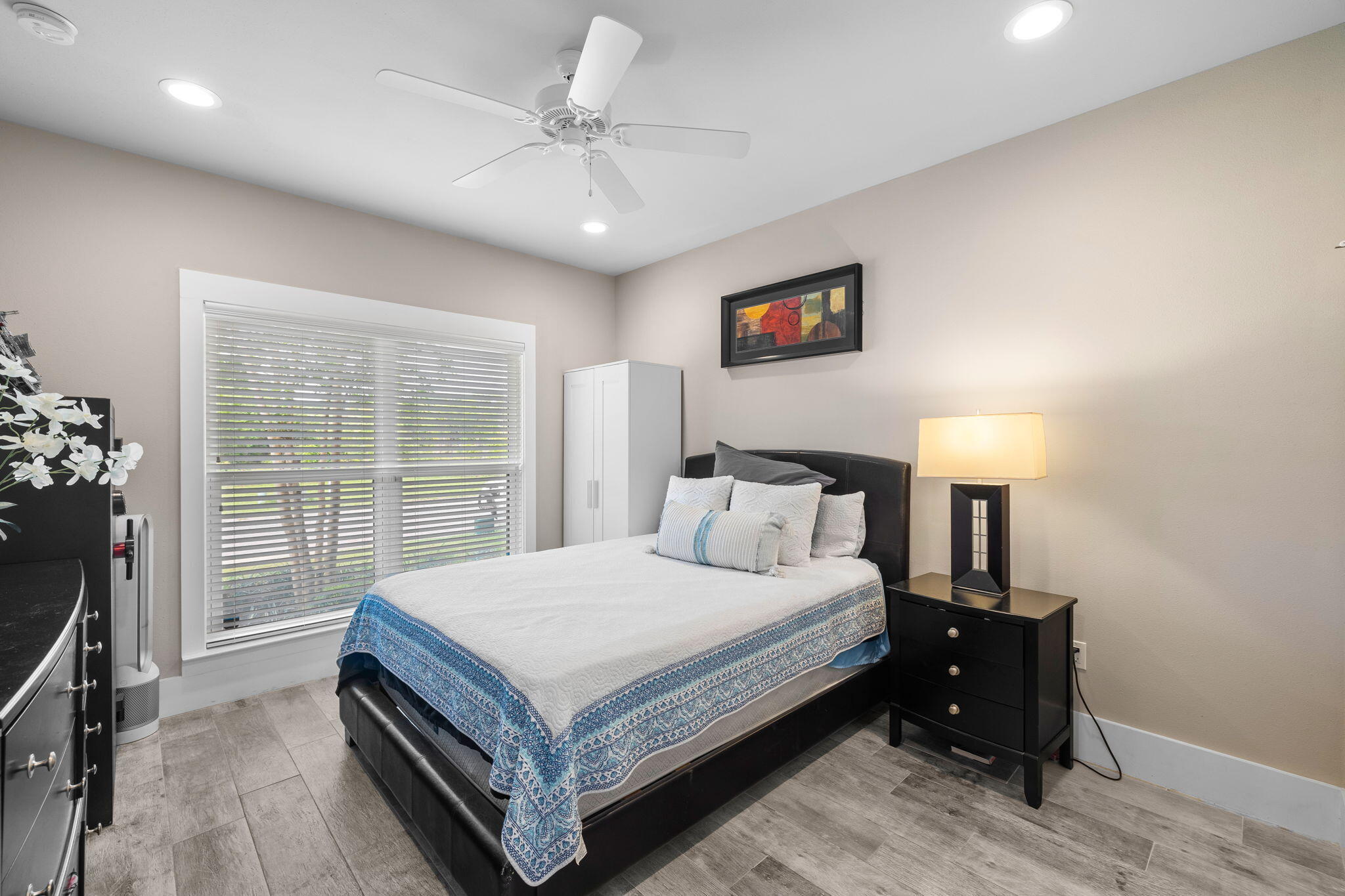 Bedroom with a black bed, blue patterned coverlet, and large window with white blinds.