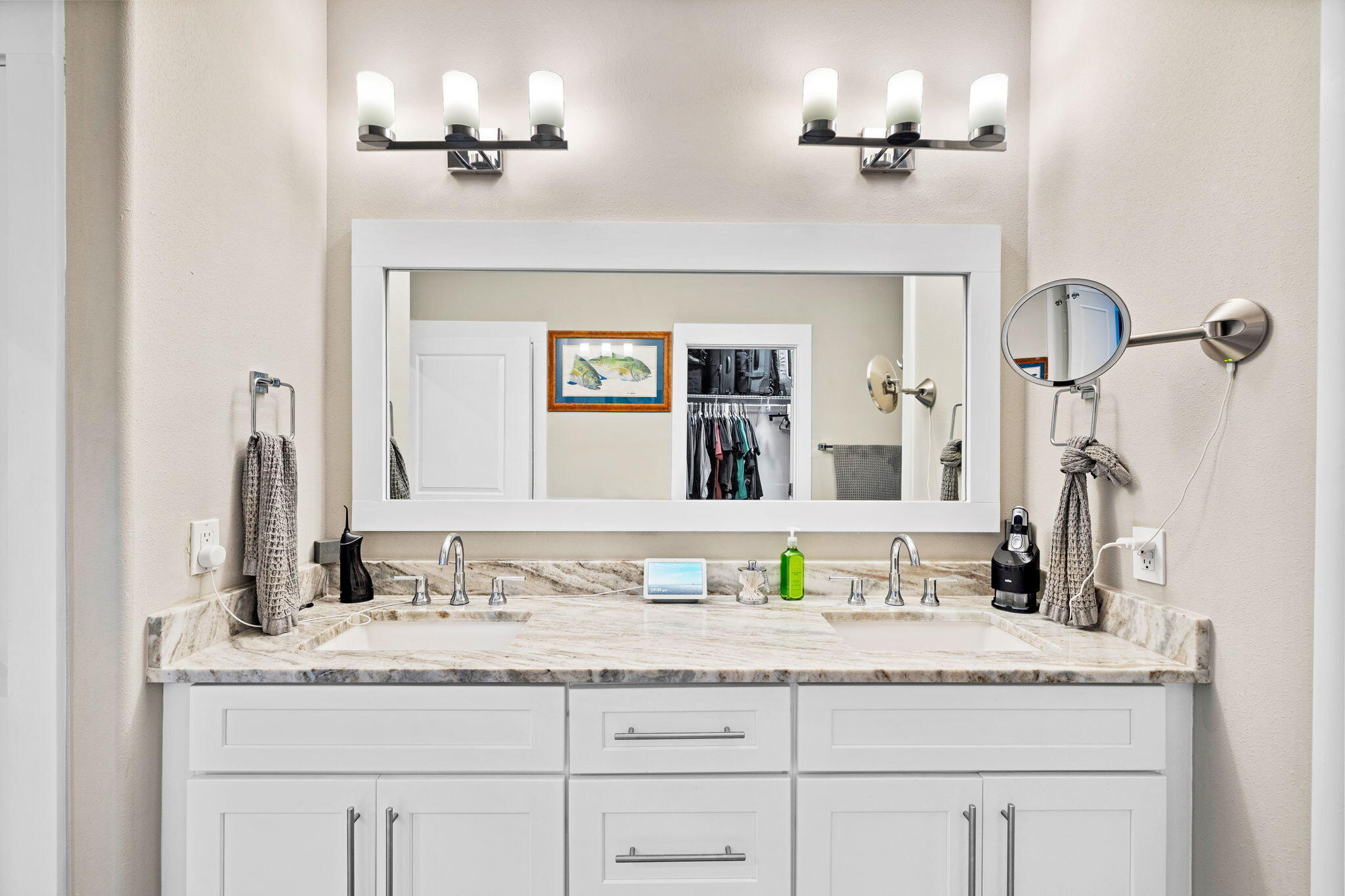 Bathroom with a double-sink vanity, white cabinetry, and a wide mirror above a veined stone countertop.