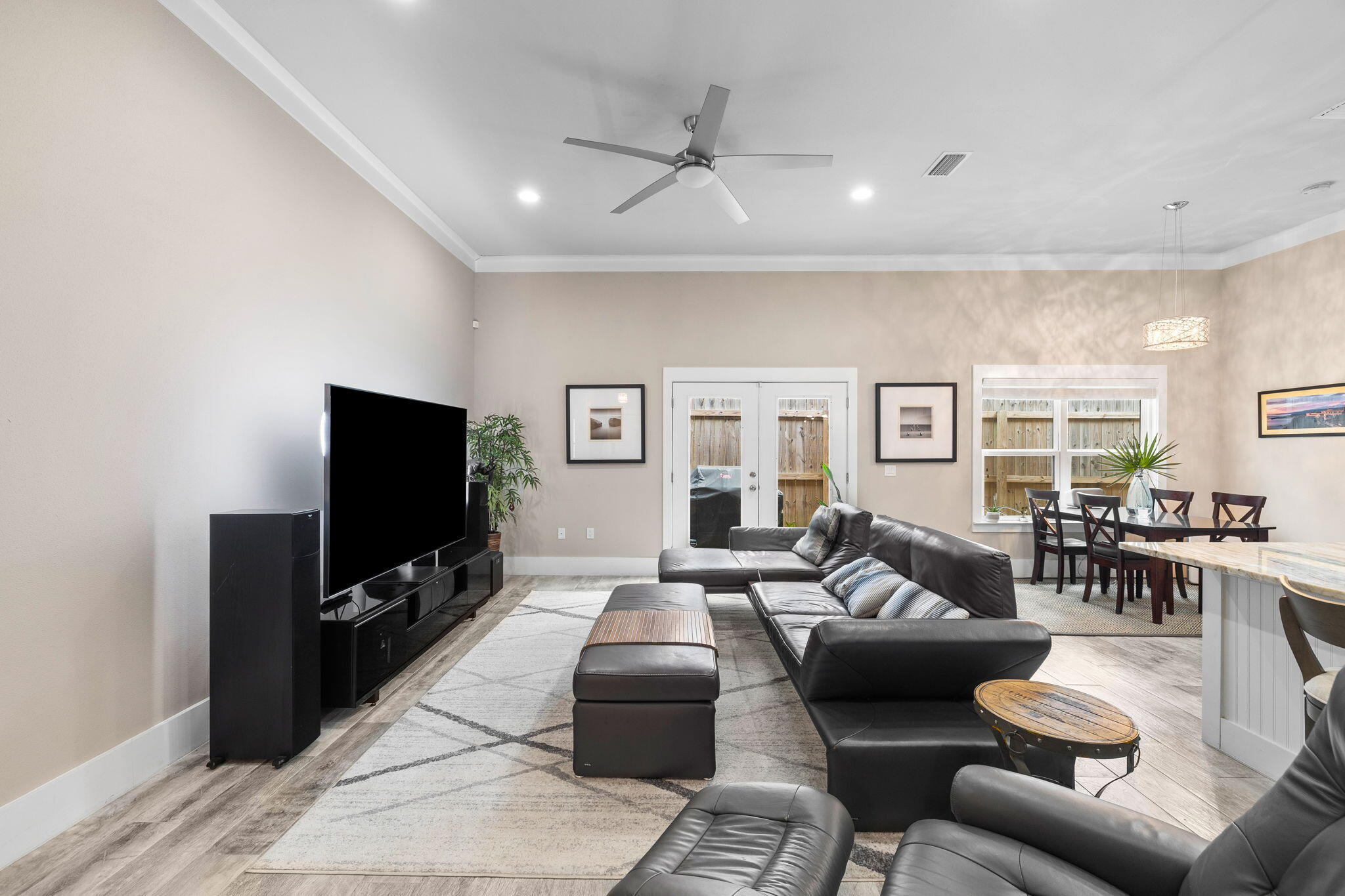 Living room with a black leather sectional, large TV, ceiling fan, and adjoining dining area.