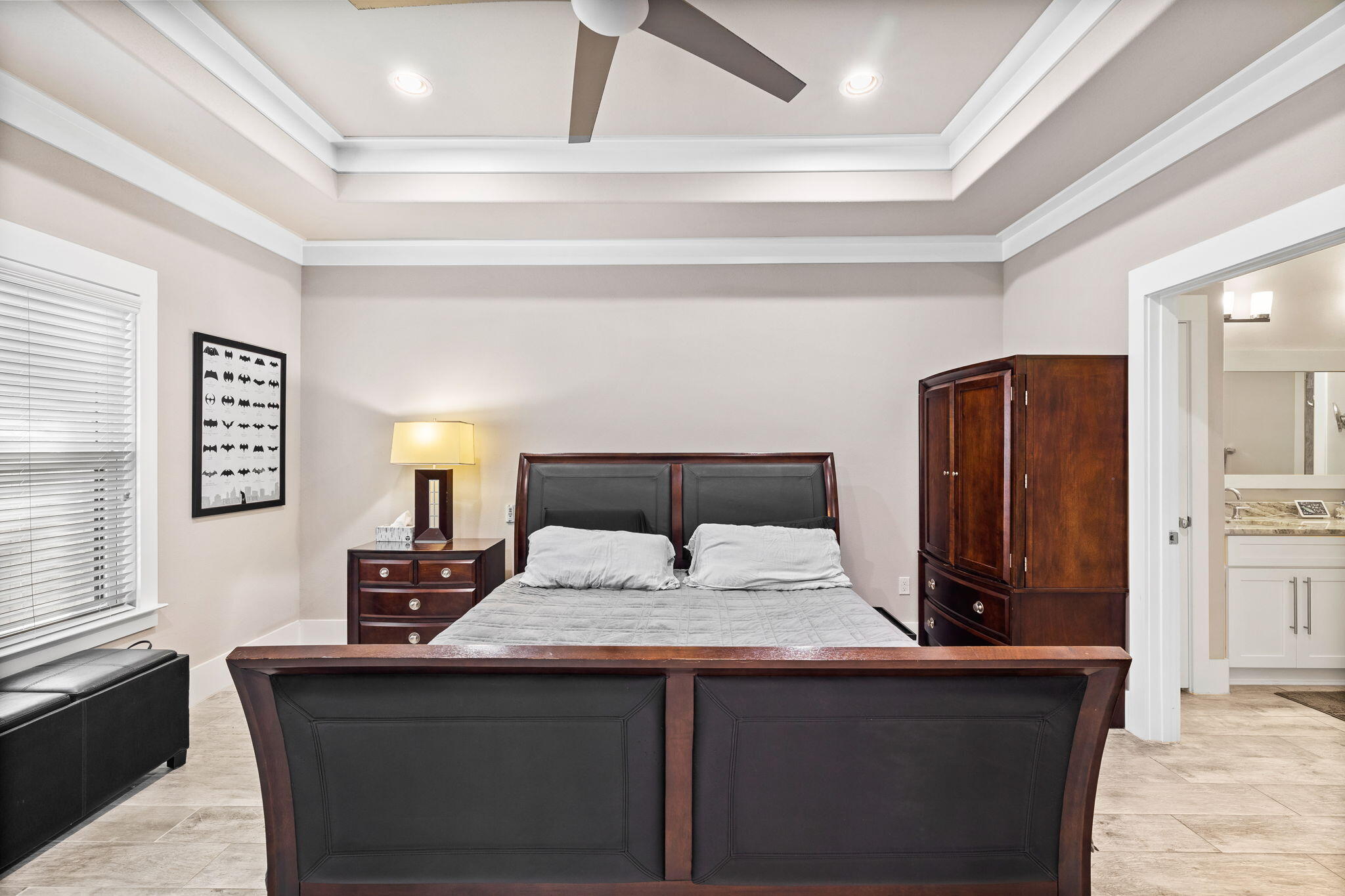 Bedroom with a dark wood bed and matching armoire beneath a tray ceiling with a ceiling fan.