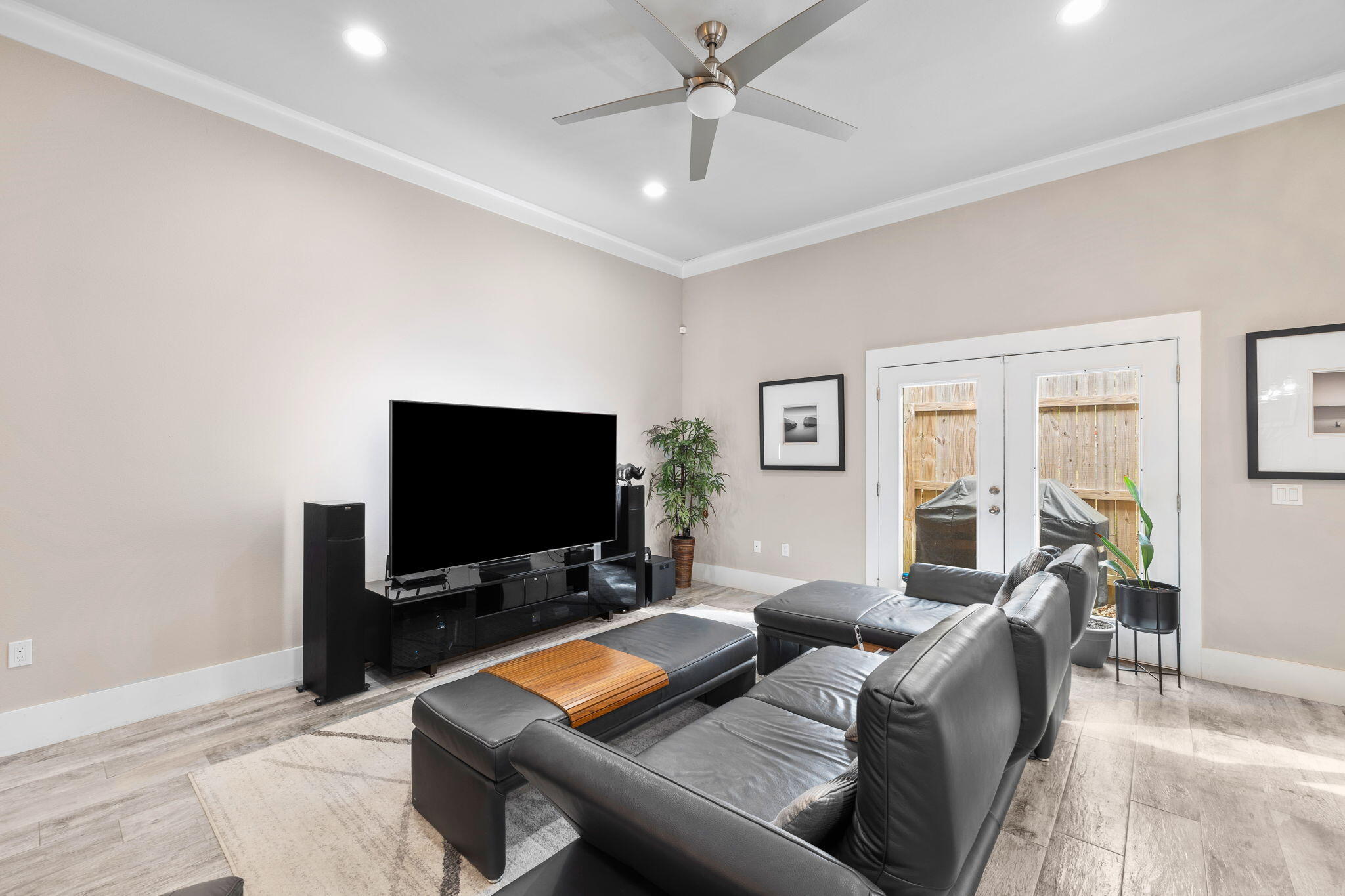 Living room with a black leather sectional, large television, and glass double doors to a fenced patio.